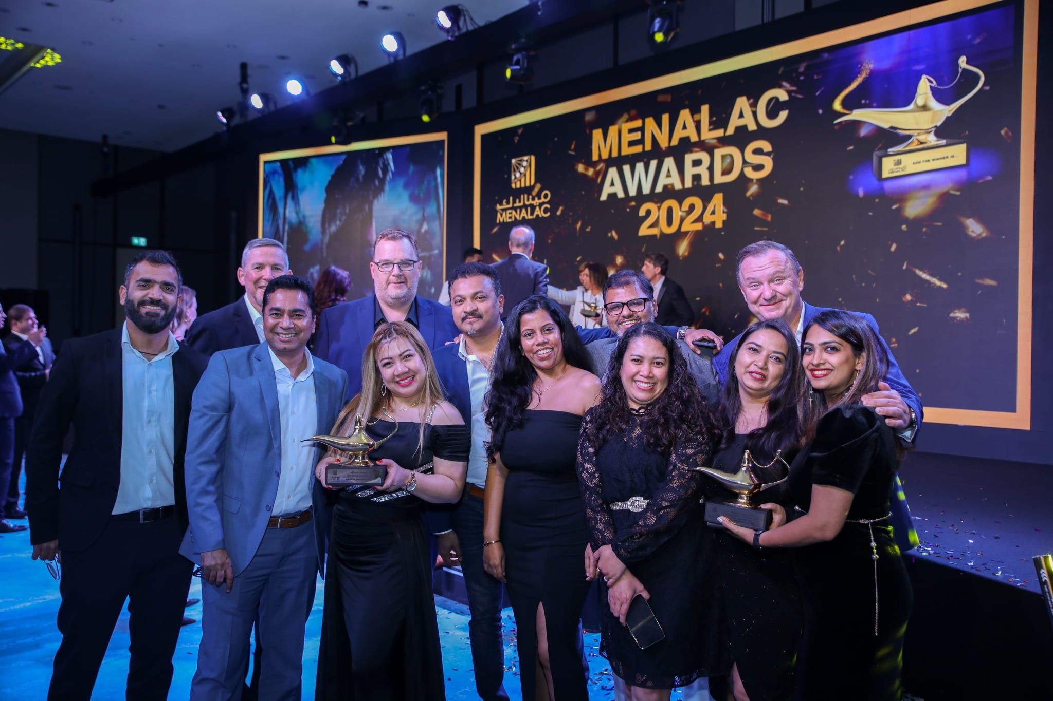 Award winners celebrating with their trophies in front of the MENALAC Awards 2024 backdrop