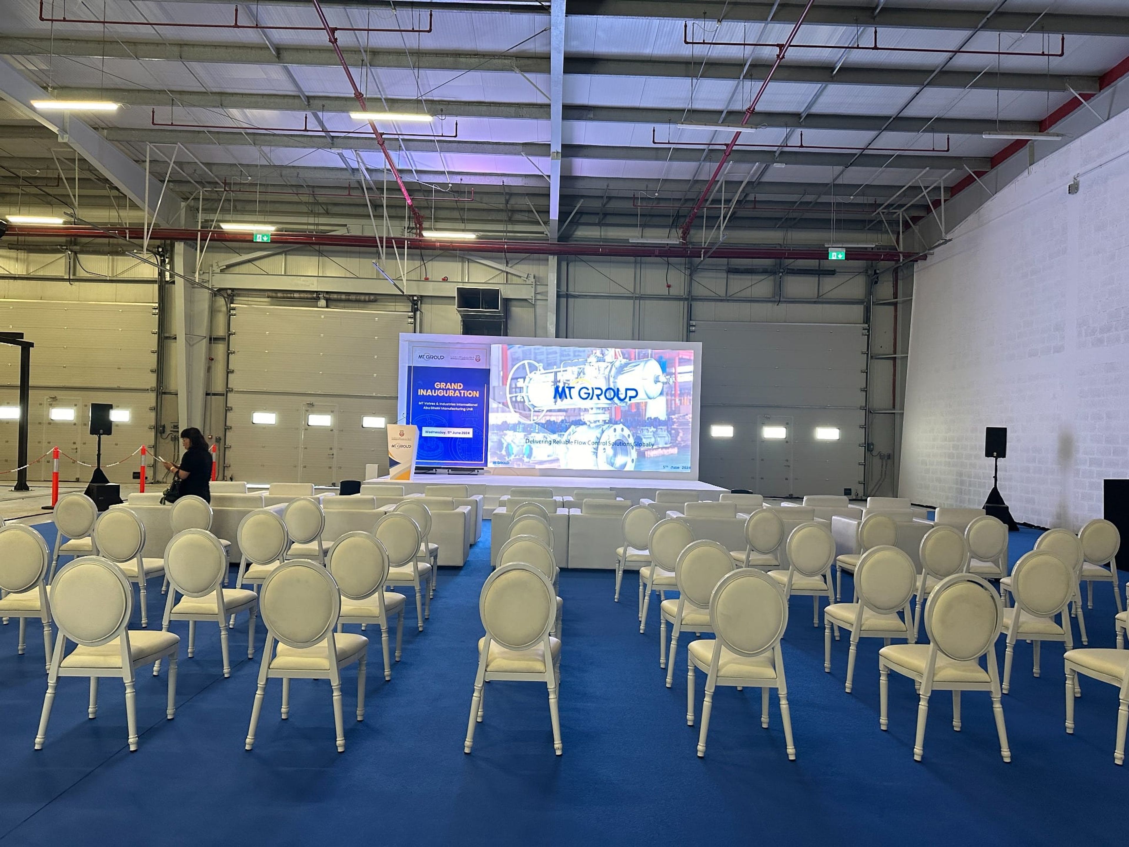 Theatre-style guest seating facing the stage screen inside the factory hall