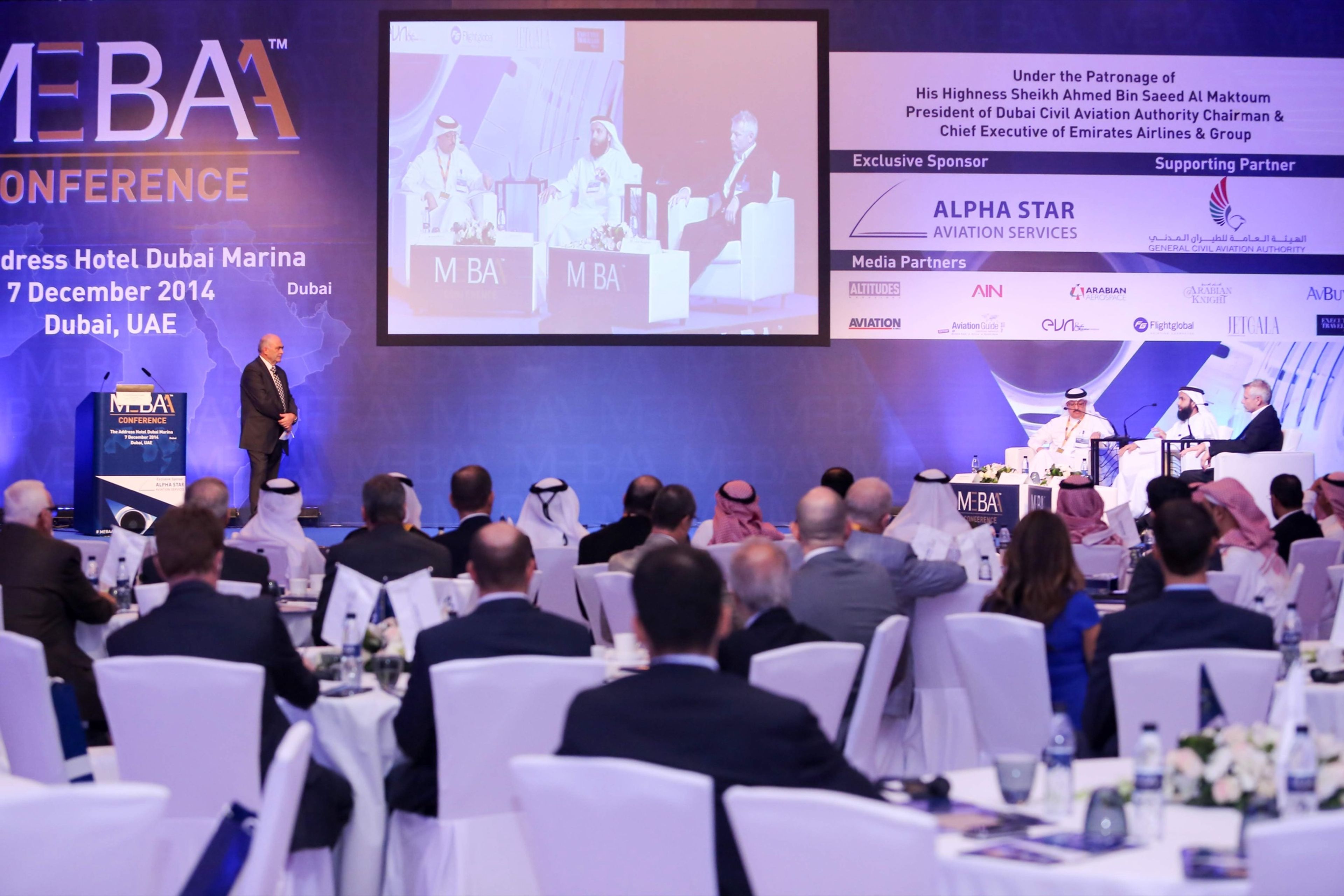 Speaker addressing delegates at a business forum with a large stage screen