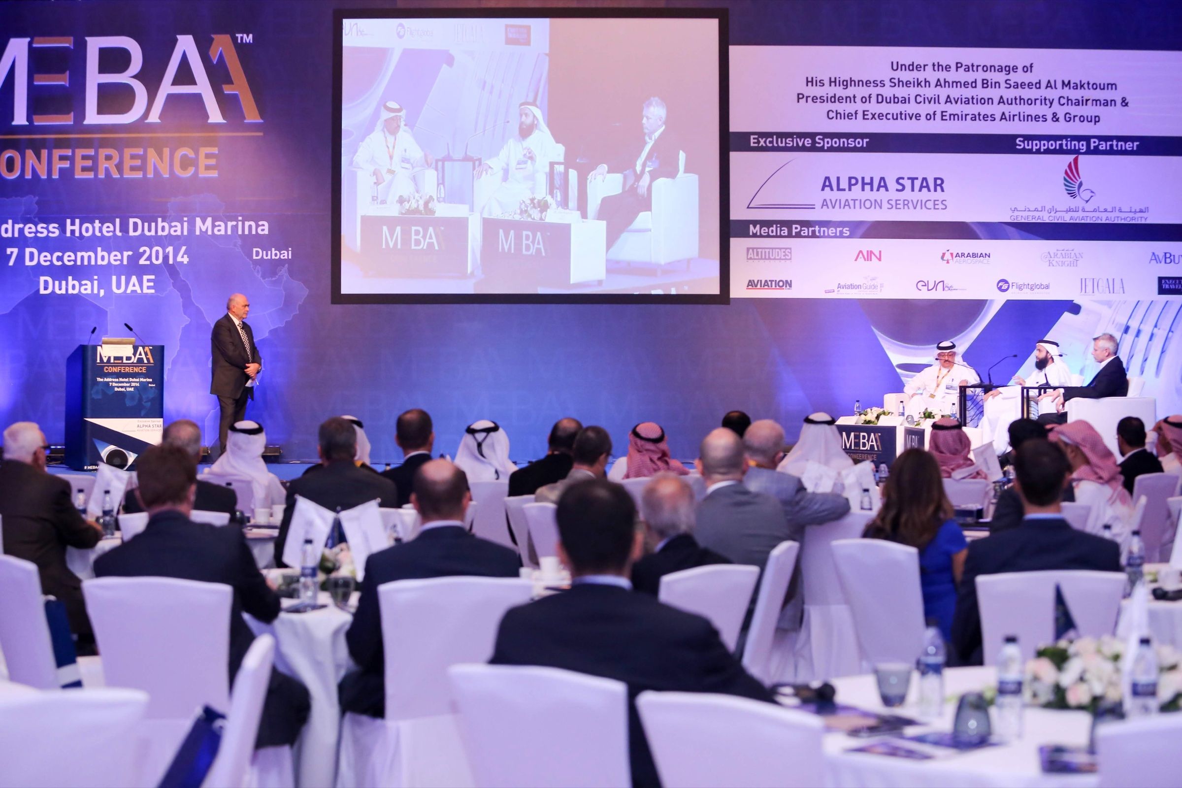 Speaker addressing delegates at a business forum with a large stage screen
