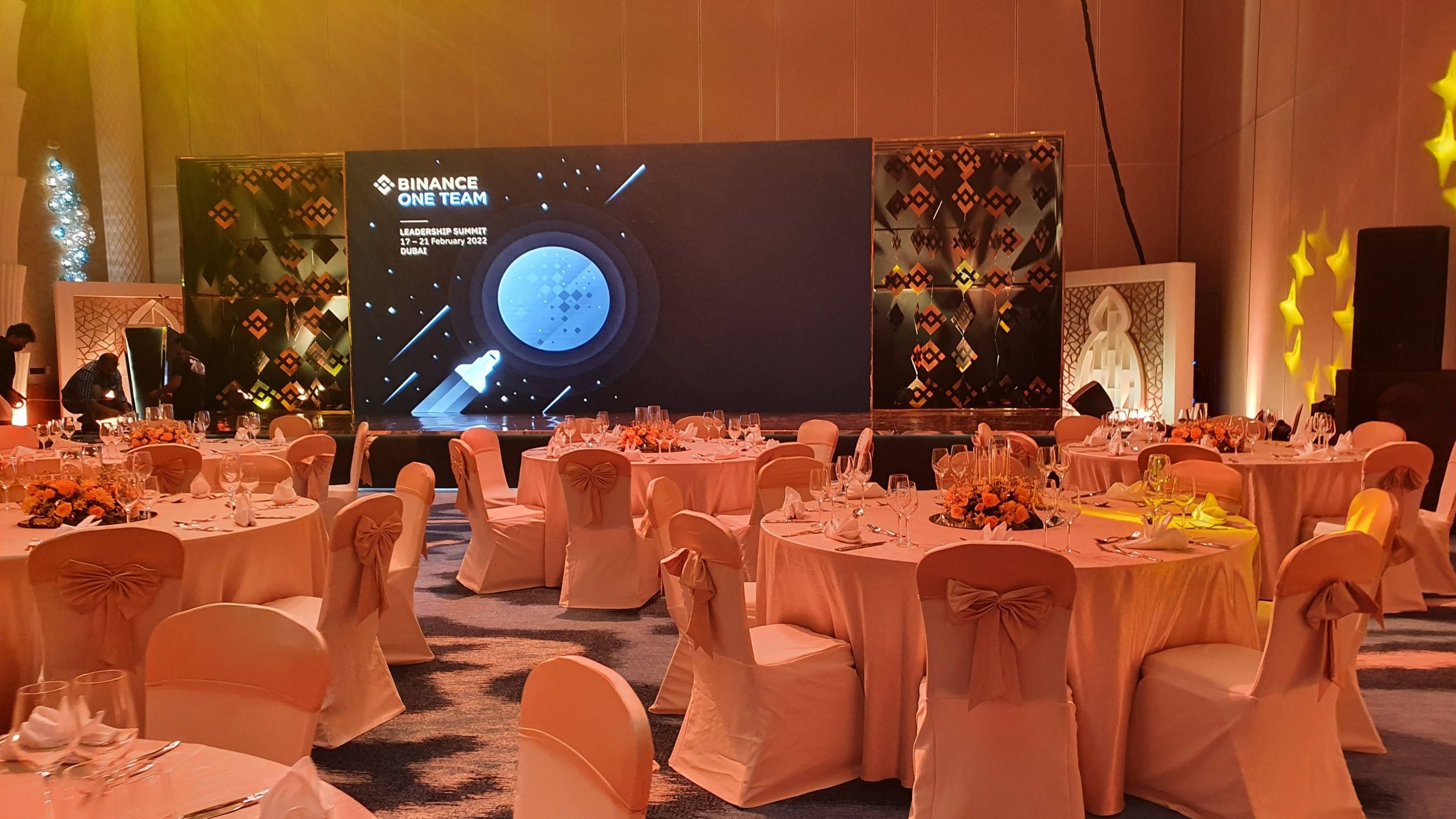 Round tables set for a formal corporate gala dinner with stage in the background.