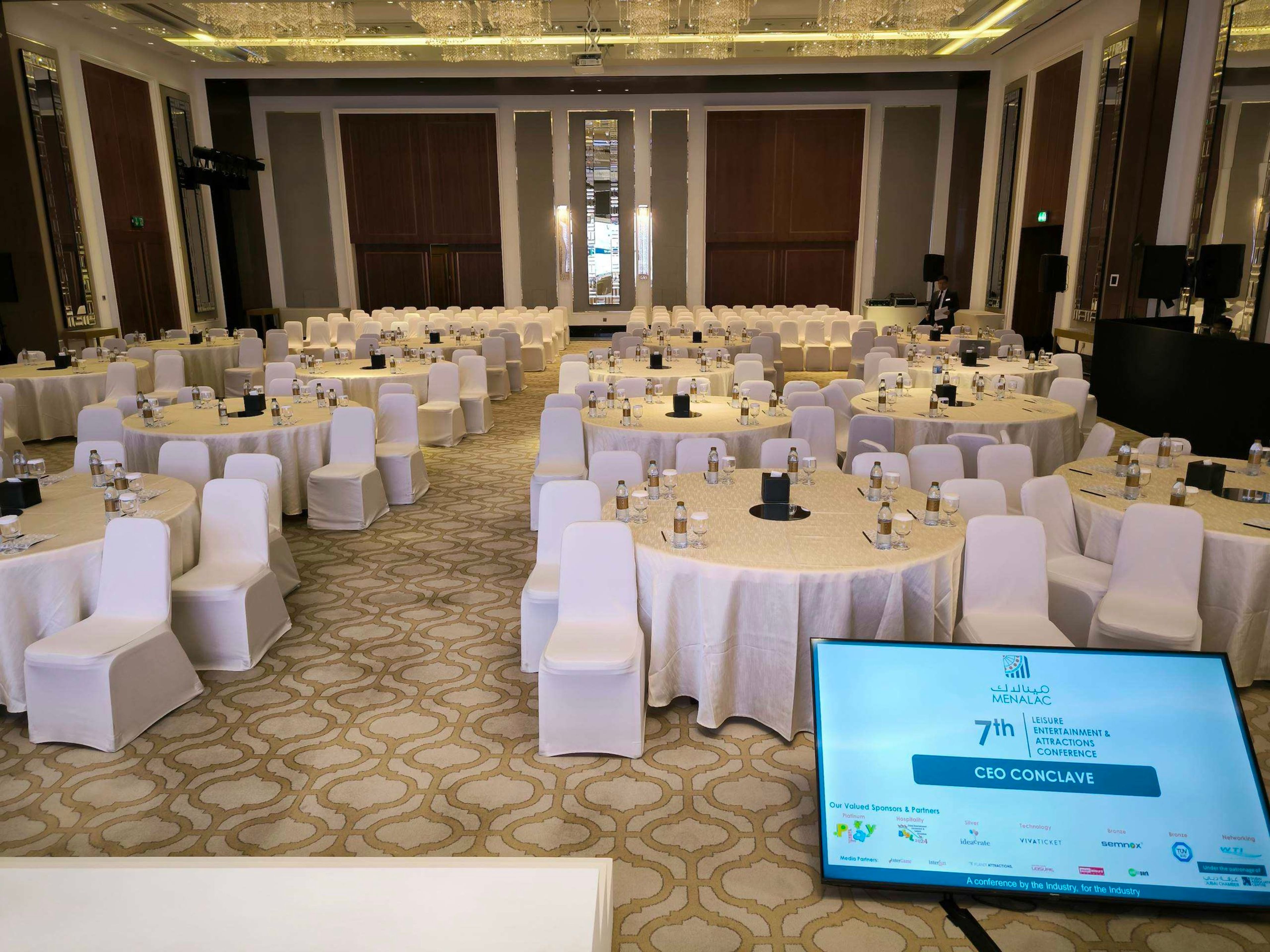 Hotel ballroom with round tables and white chairs set for a banquet
