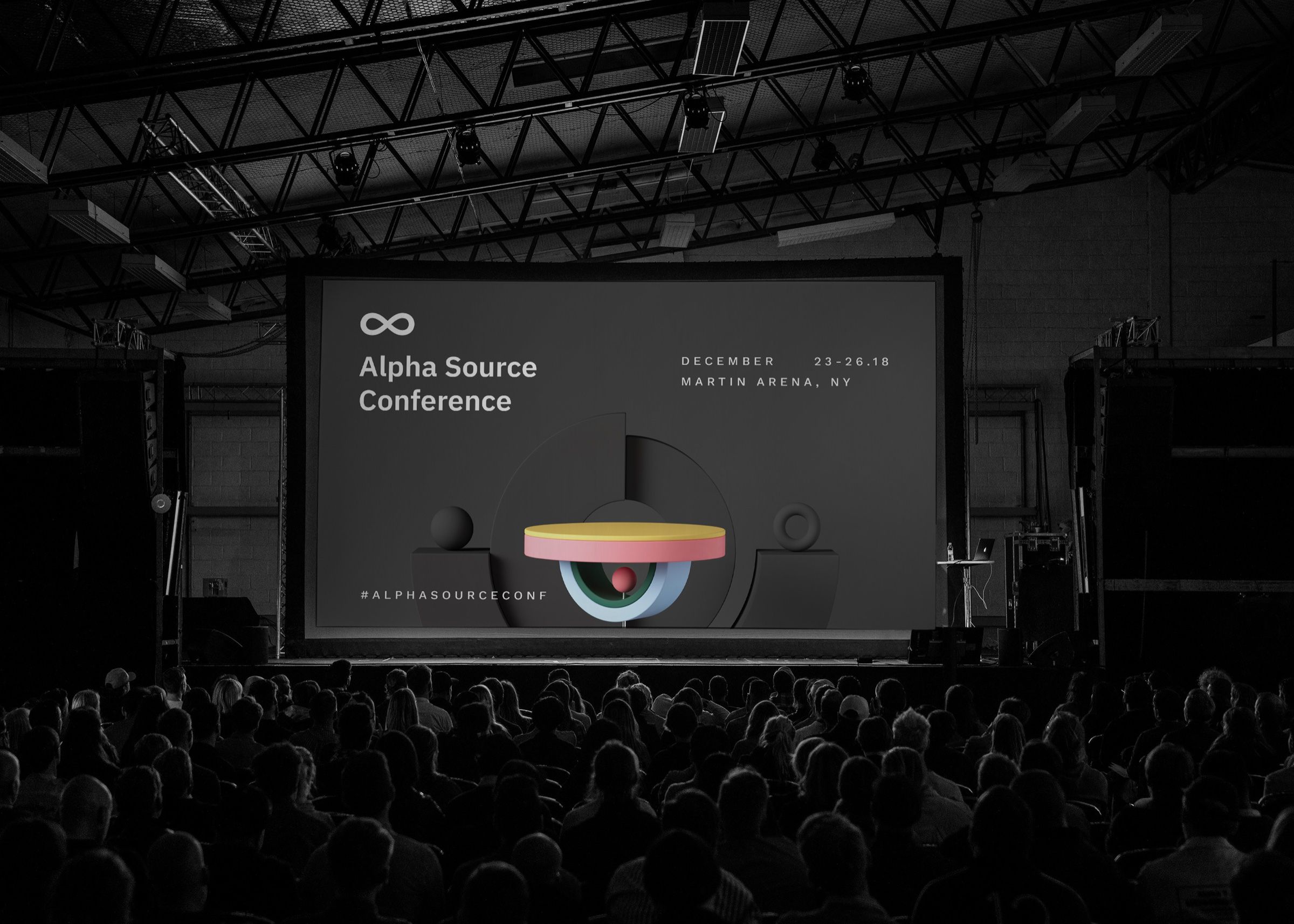 Audience in a dark auditorium facing a conference stage screen