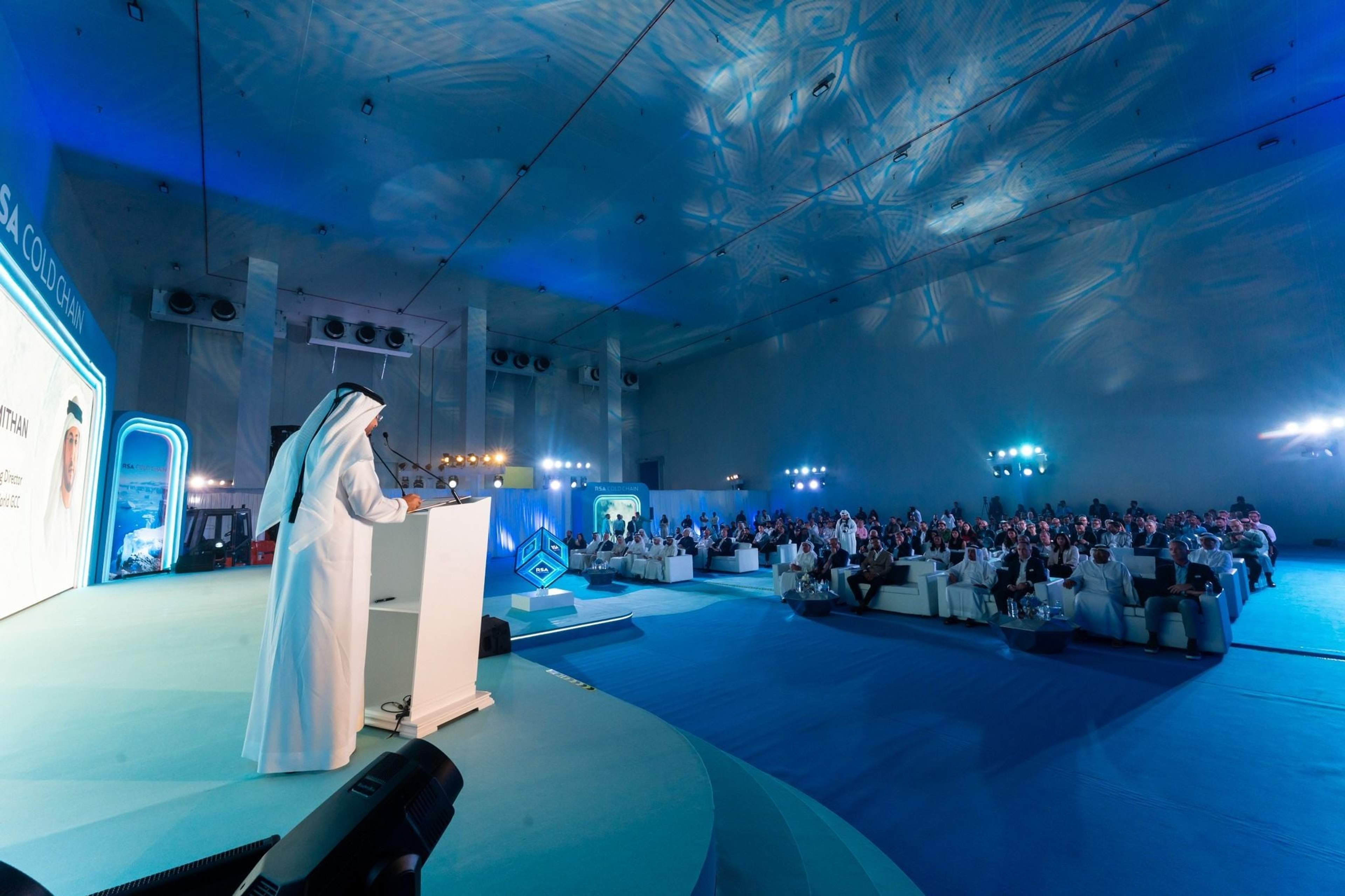 Speaker on stage at the RSA Cold Chain facility launch in Jebel Ali, Dubai, with a seated audience under blue light and snowflake ceiling projections