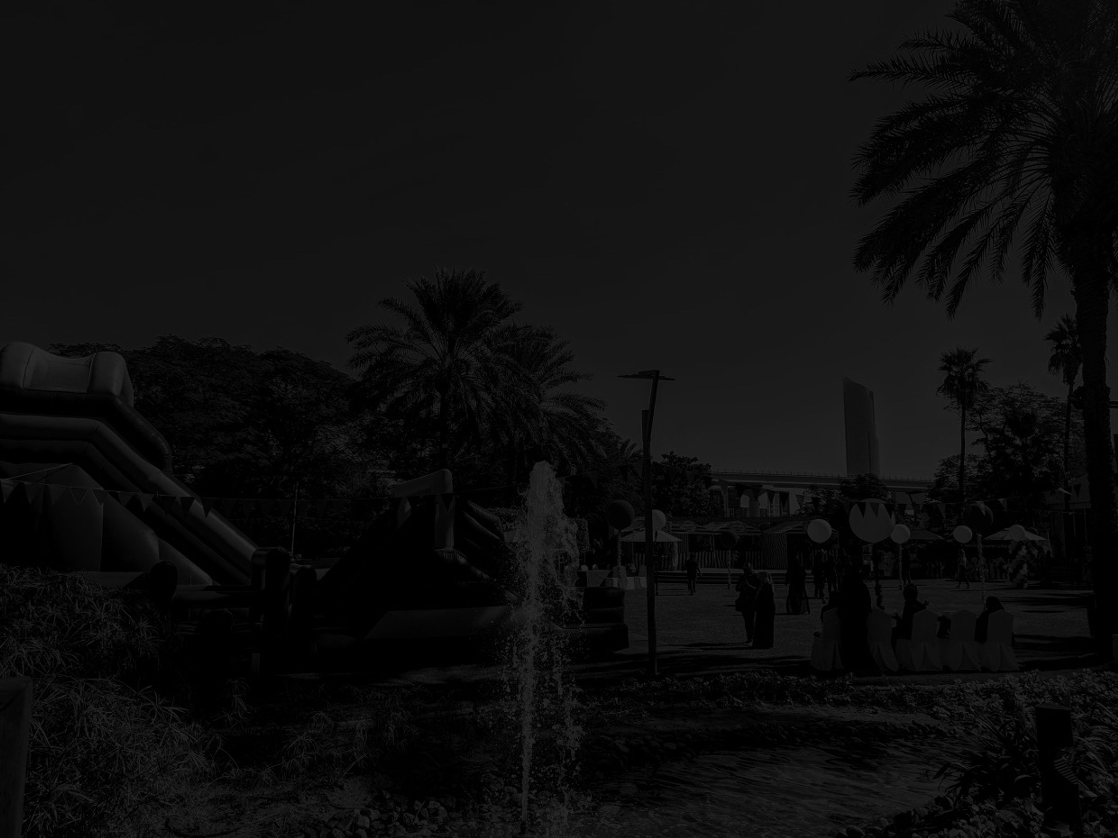Inflatables and carnival stalls set up among palm trees and a fountain for a corporate family day in a Dubai park