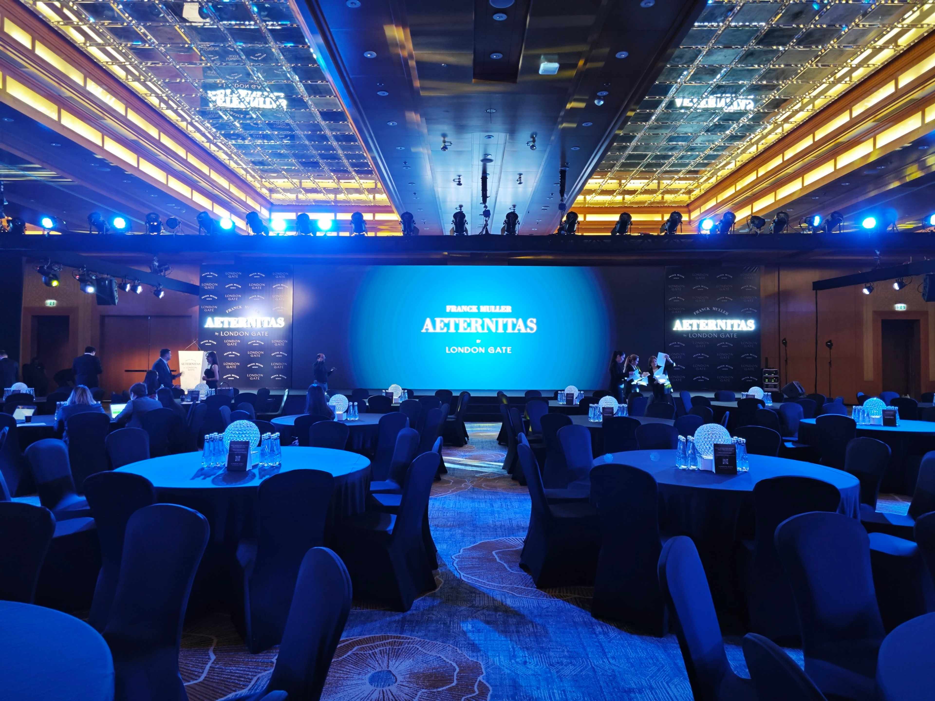 Hotel ballroom set for a corporate gala dinner in Dubai, with round tables, a stage and an LED screen in blue light