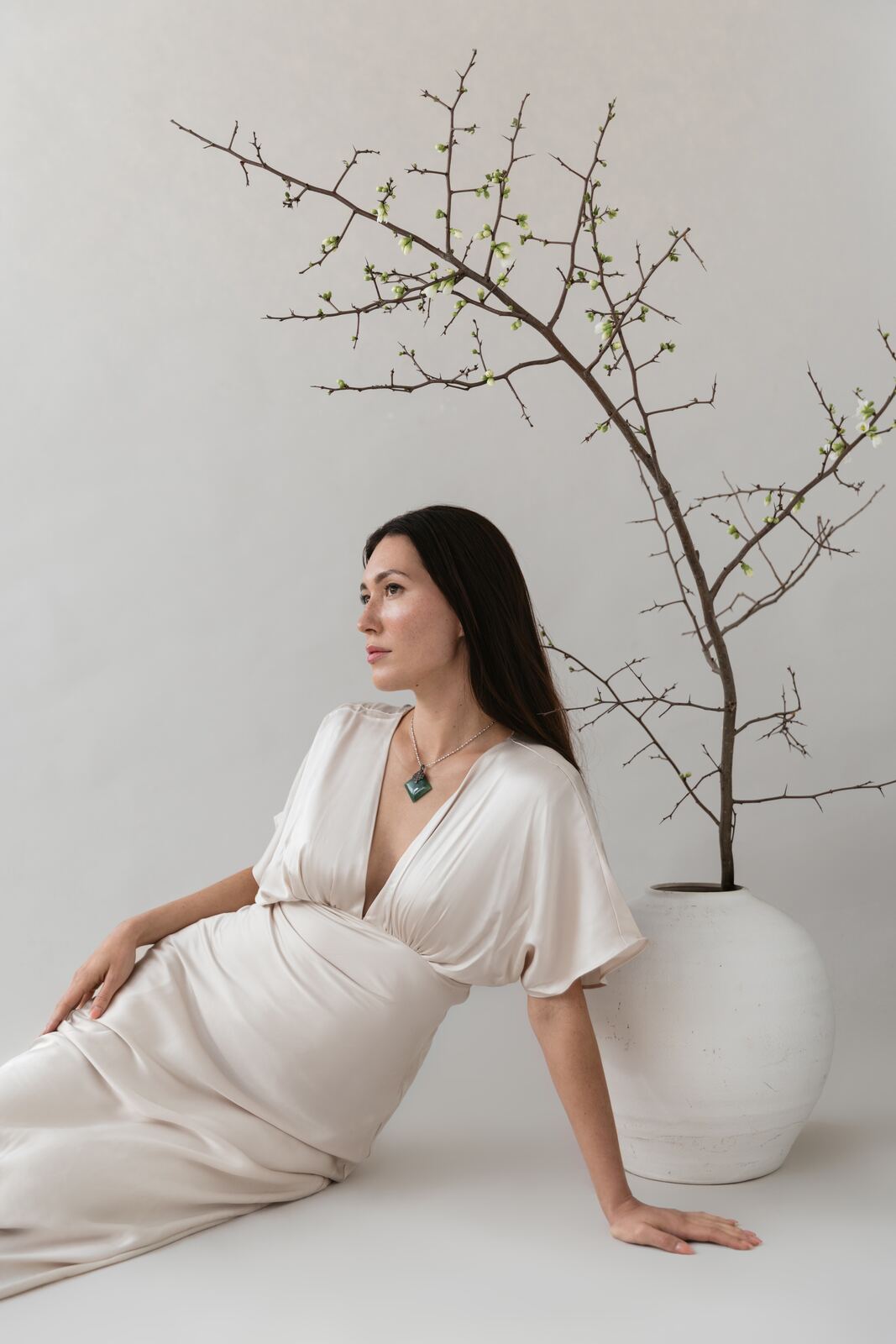 Woman in a white dress seated beside a flowering branch
