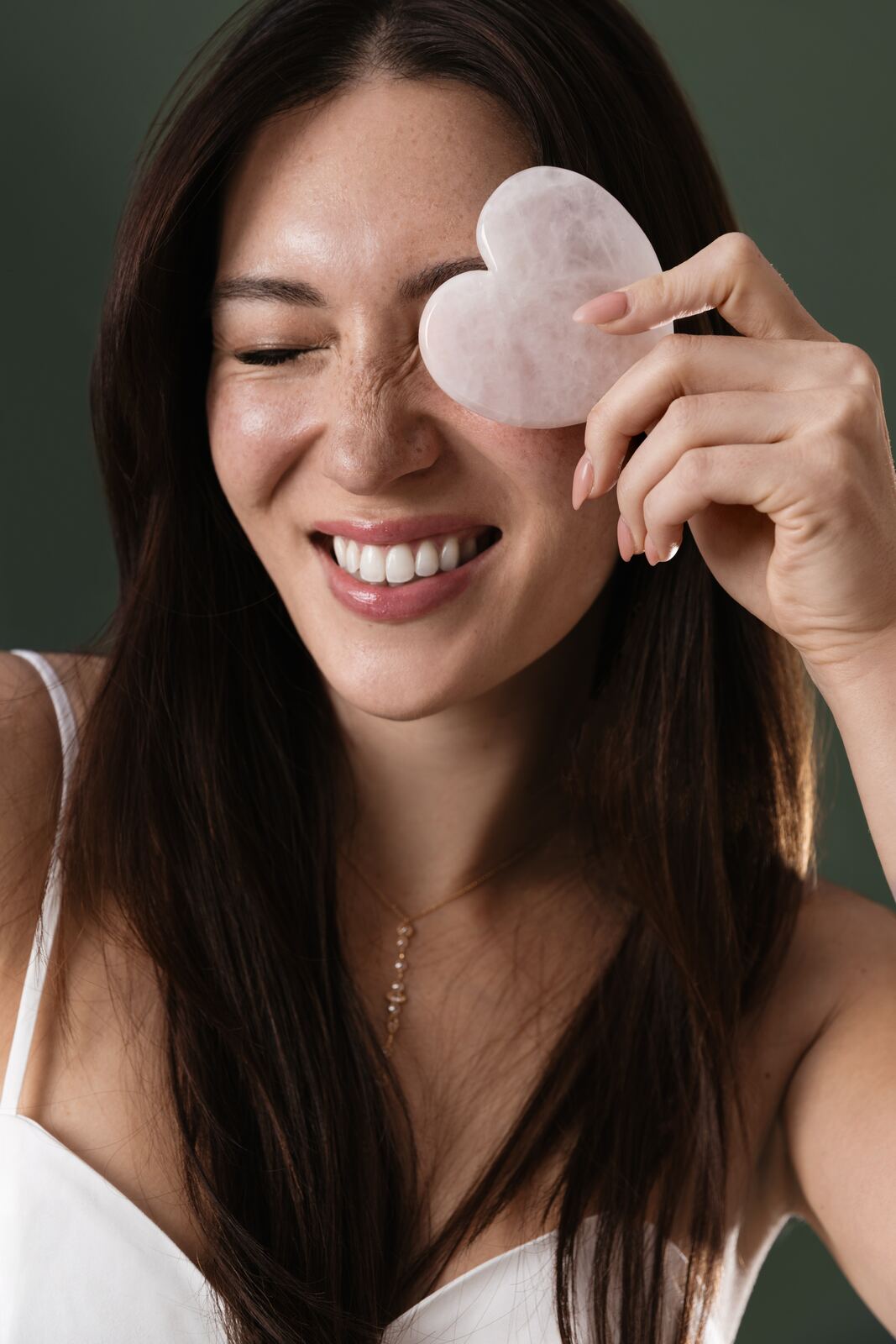 Smiling woman holding a heart-shaped rose quartz gua sha stone