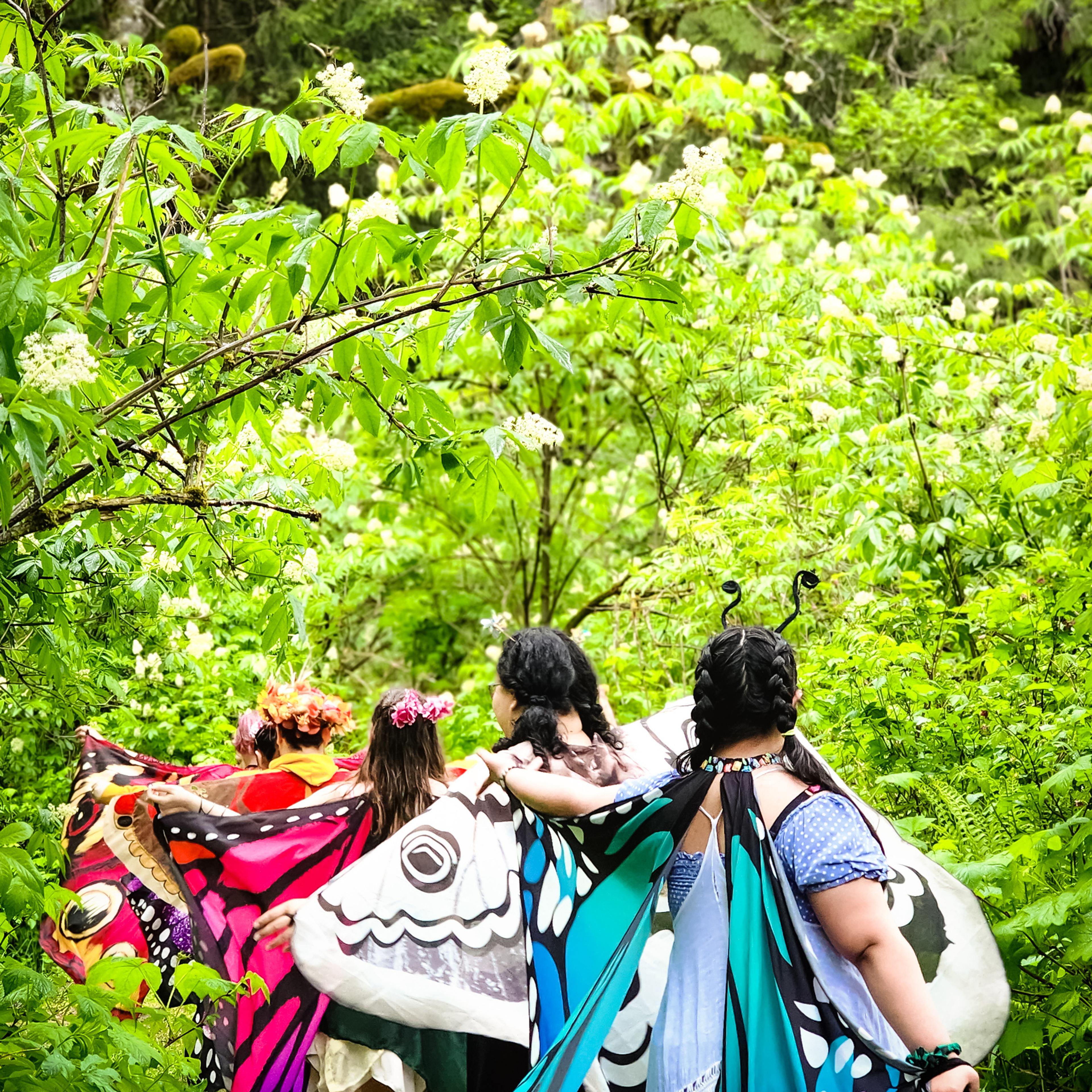 A row of people in butterfly wings walking away through lush green foliage.