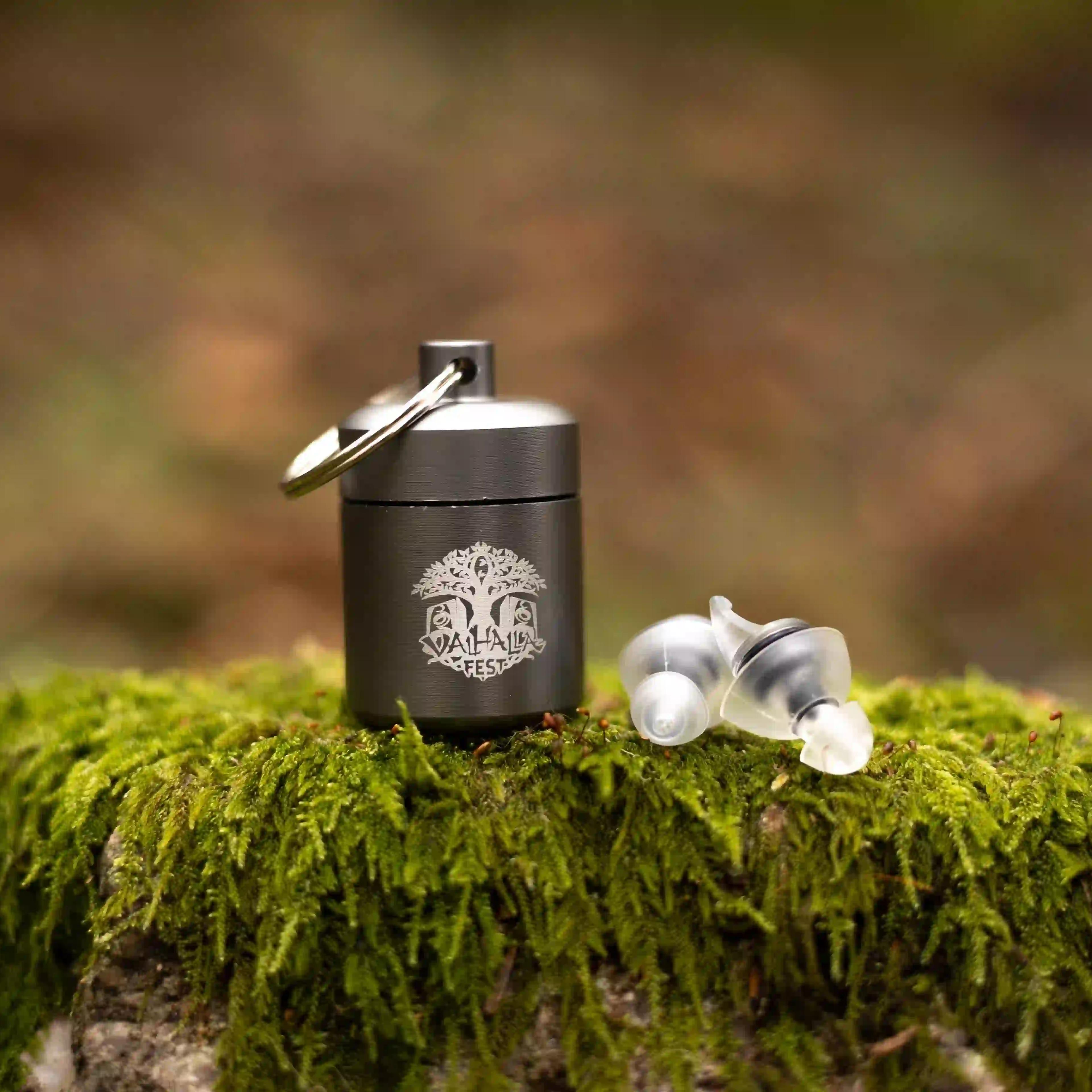 ValhallaFest branded keychain earplugs container with earbuds on moss