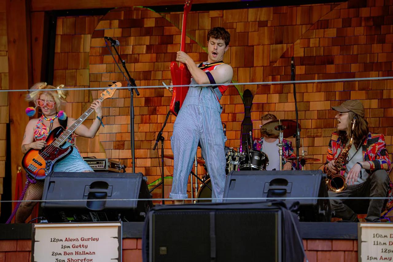 Live band with bass, vocals, drums, and saxophone on AgeHa stage.