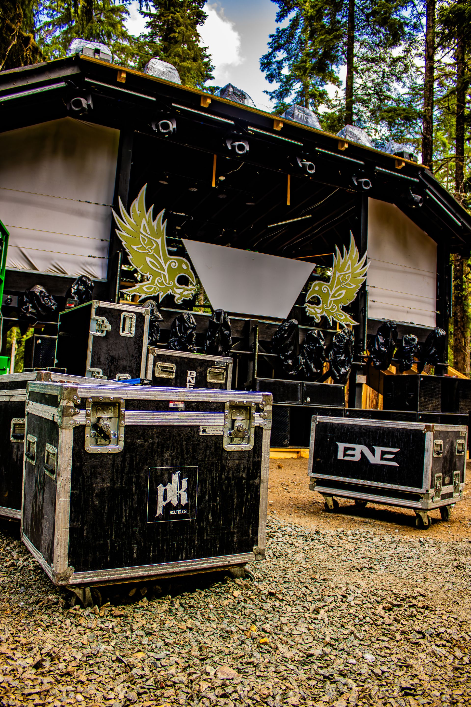 PK Sound and BNE road cases in front of the decorated festival stage during daytime setup in the forest.