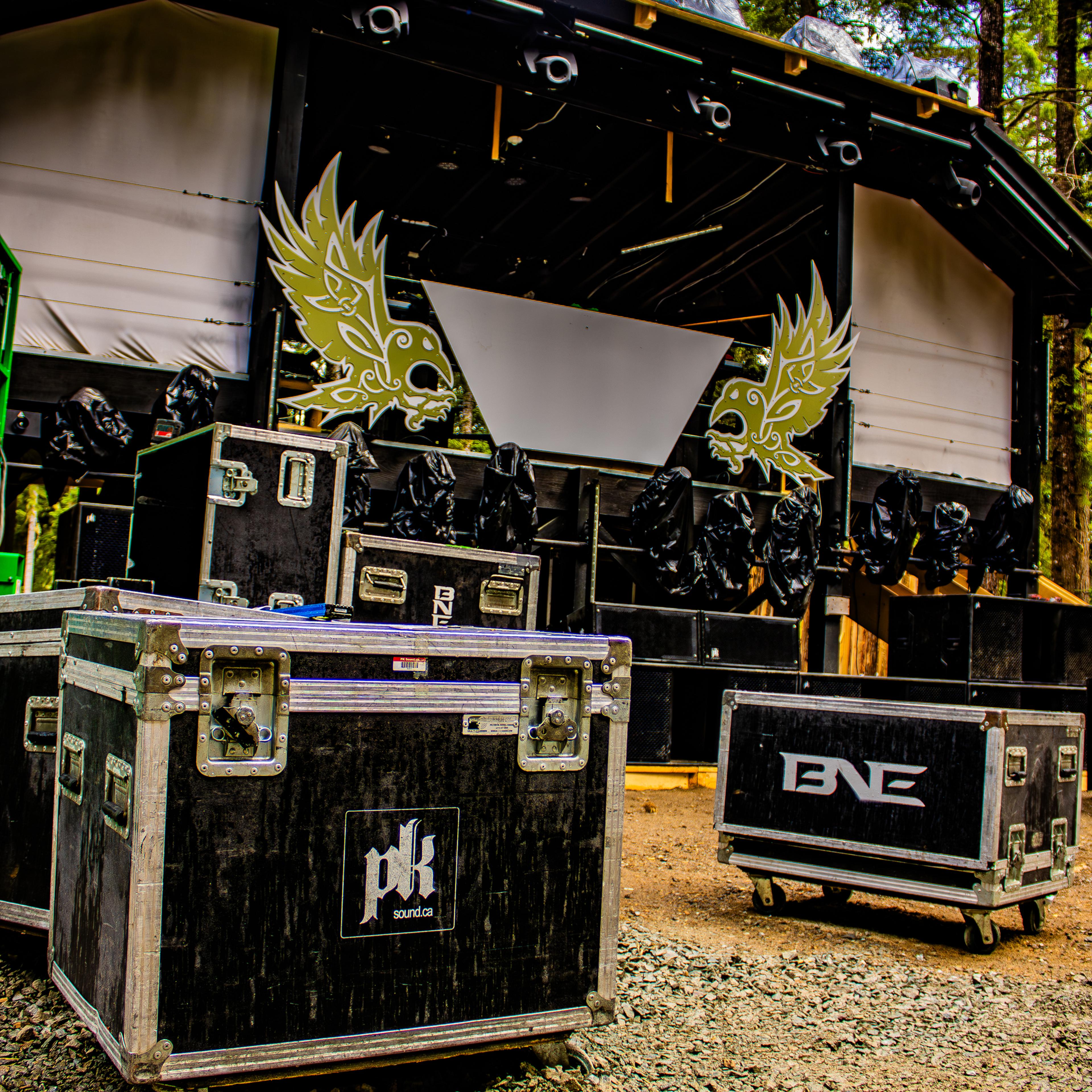 PK Sound and BNE road cases in front of the decorated festival stage during daytime setup in the forest.