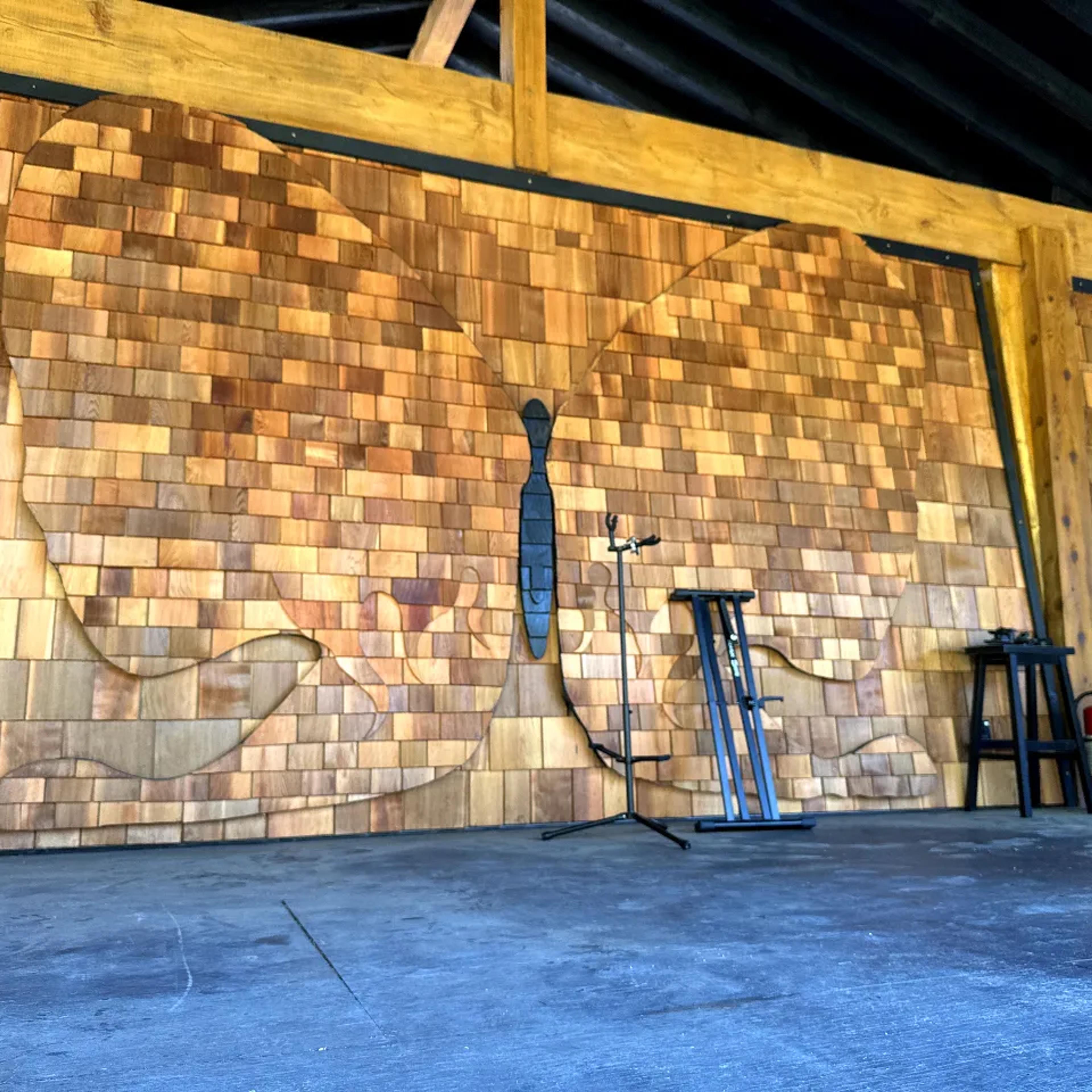 Empty AgeHa stage with backlit butterfly silhouette in cedar shingle backdrop.