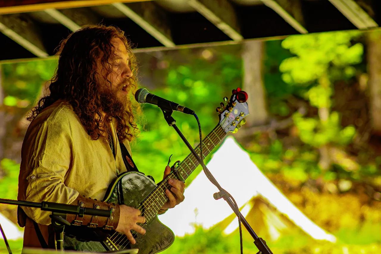 Long-haired musician singing and playing guitar at AgeHa daytime performance.