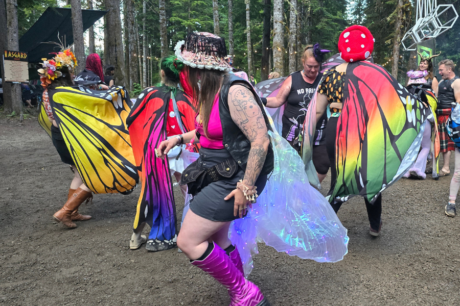Festival-goers in colorful butterfly wings and fairy costumes dancing in a forest clearing at ValhallaFest