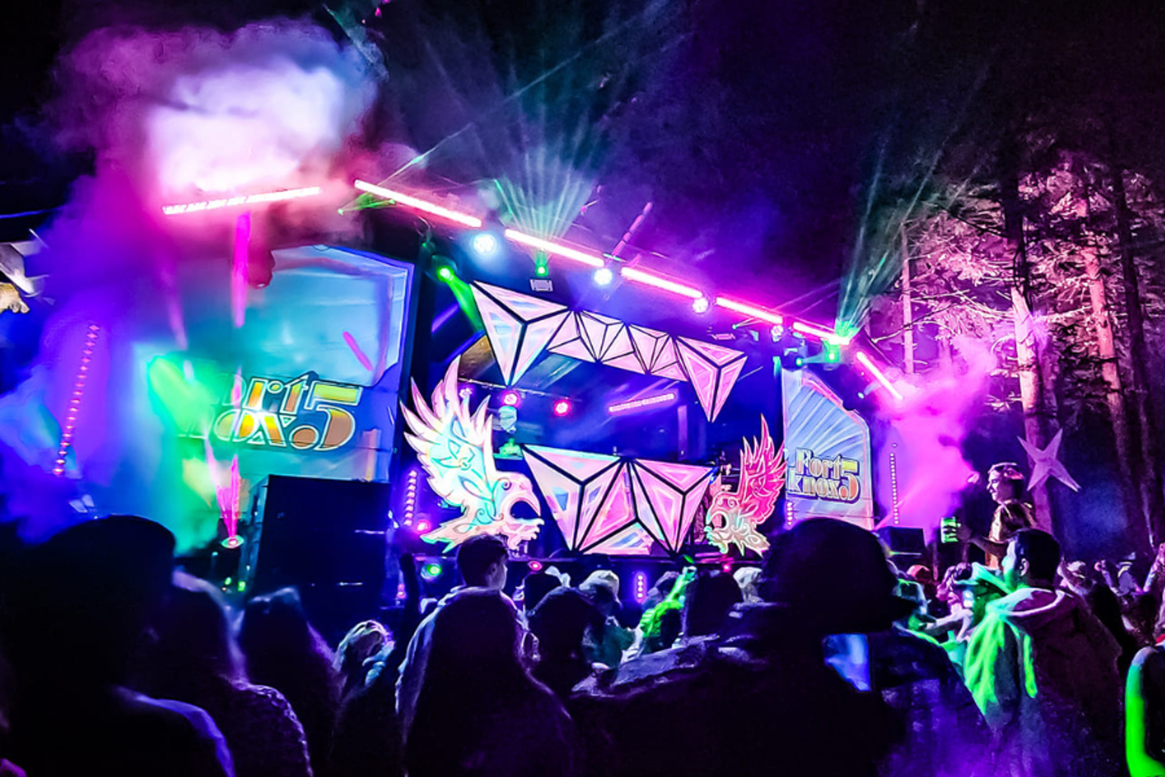 Crowd dancing in front of a neon-lit stage with lasers and fog at ValhallaFest
