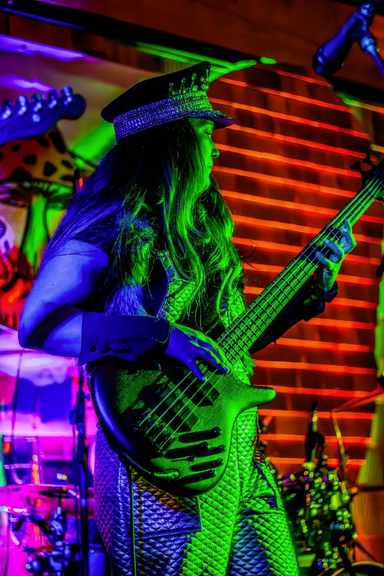 Bass guitarist in sparkly hat performing under neon green lighting performing on AgeHa stage.