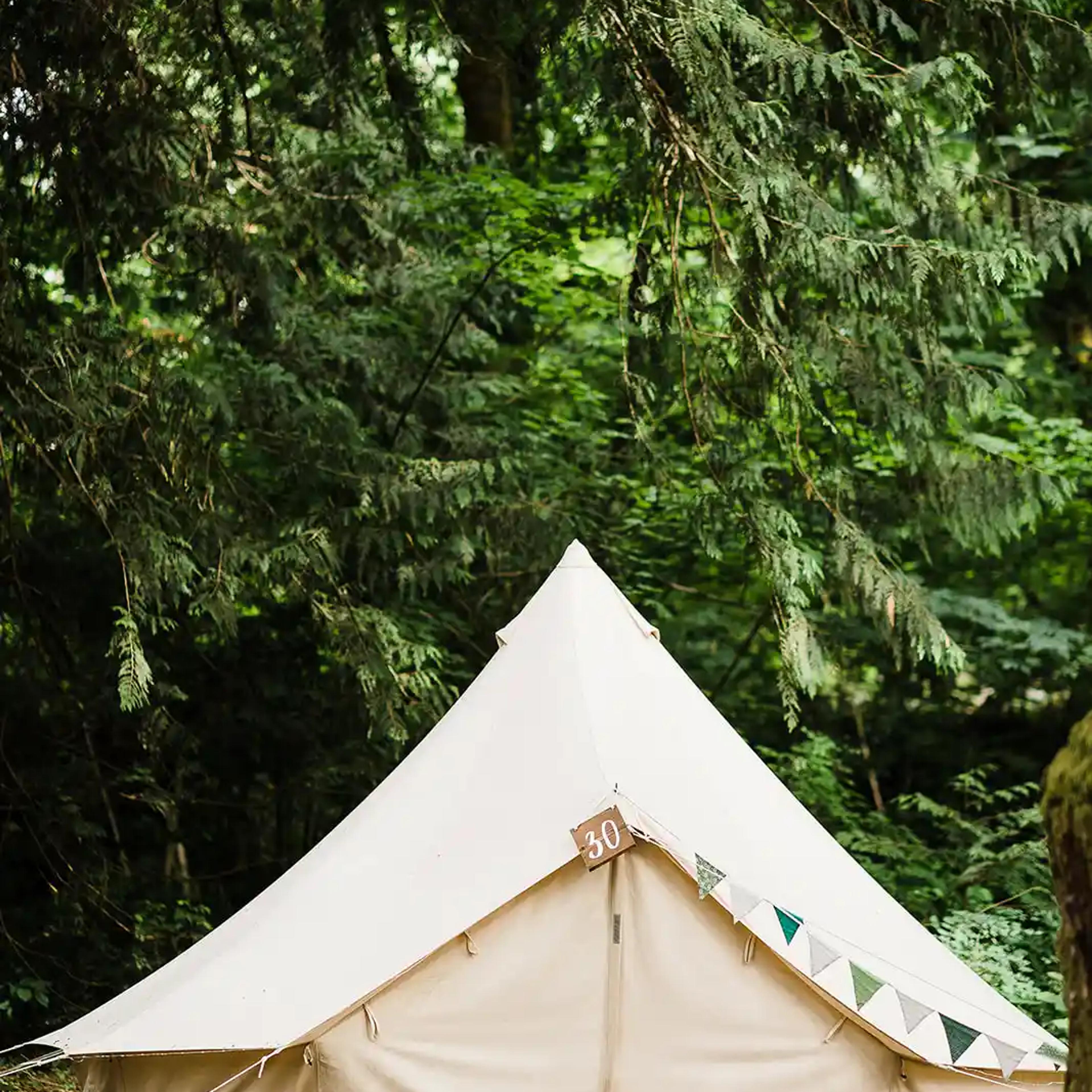 White canvas bell tent set up in a forest