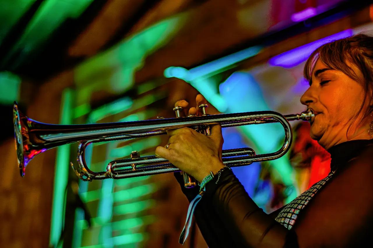 Trumpet player performing under vibrant green and purple stage lights.