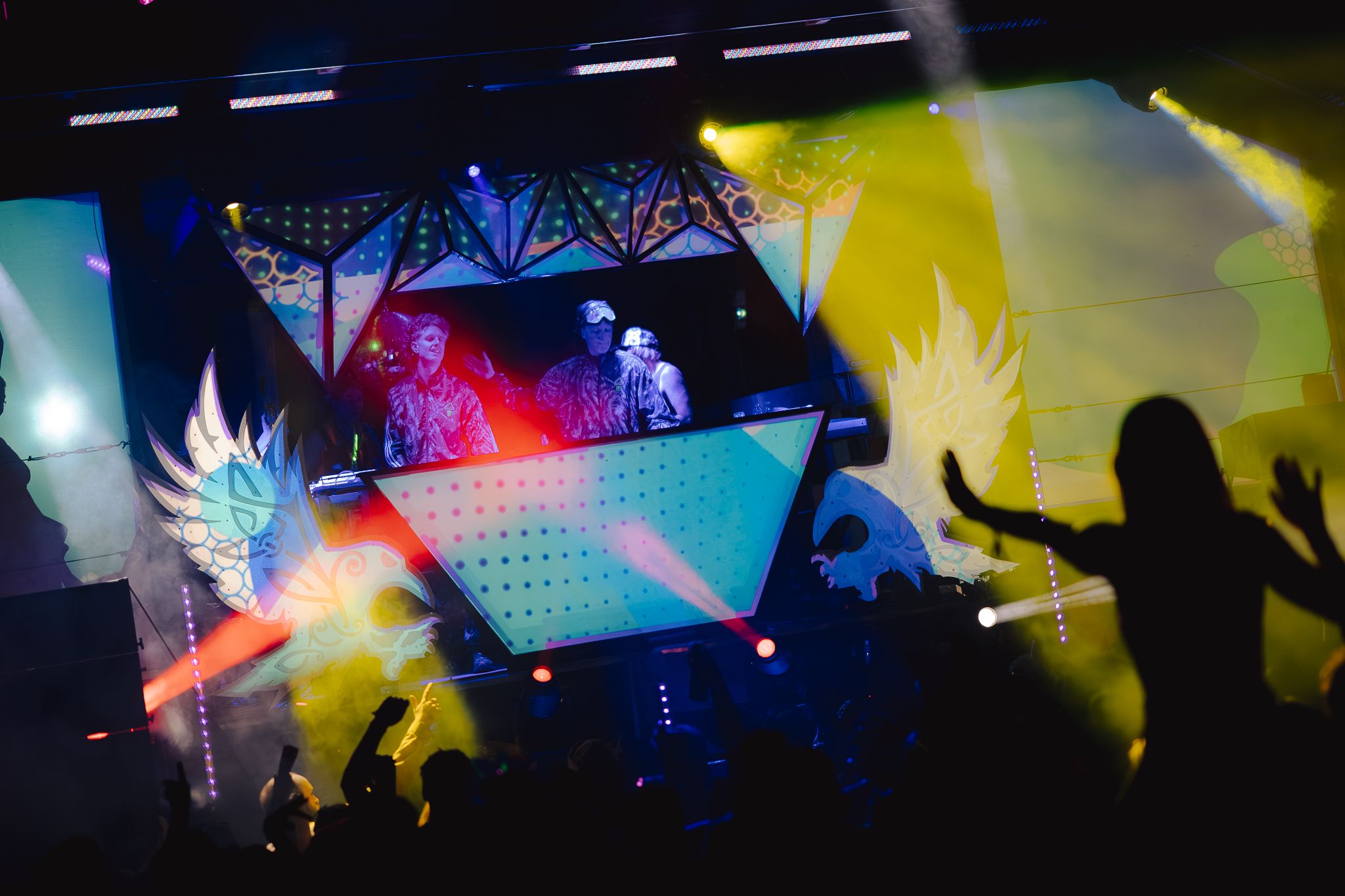 Two DJs performing on the illuminated Asgard stage with colorful lasers, smoke, and a crowd silhouetted below at ValhallaFest