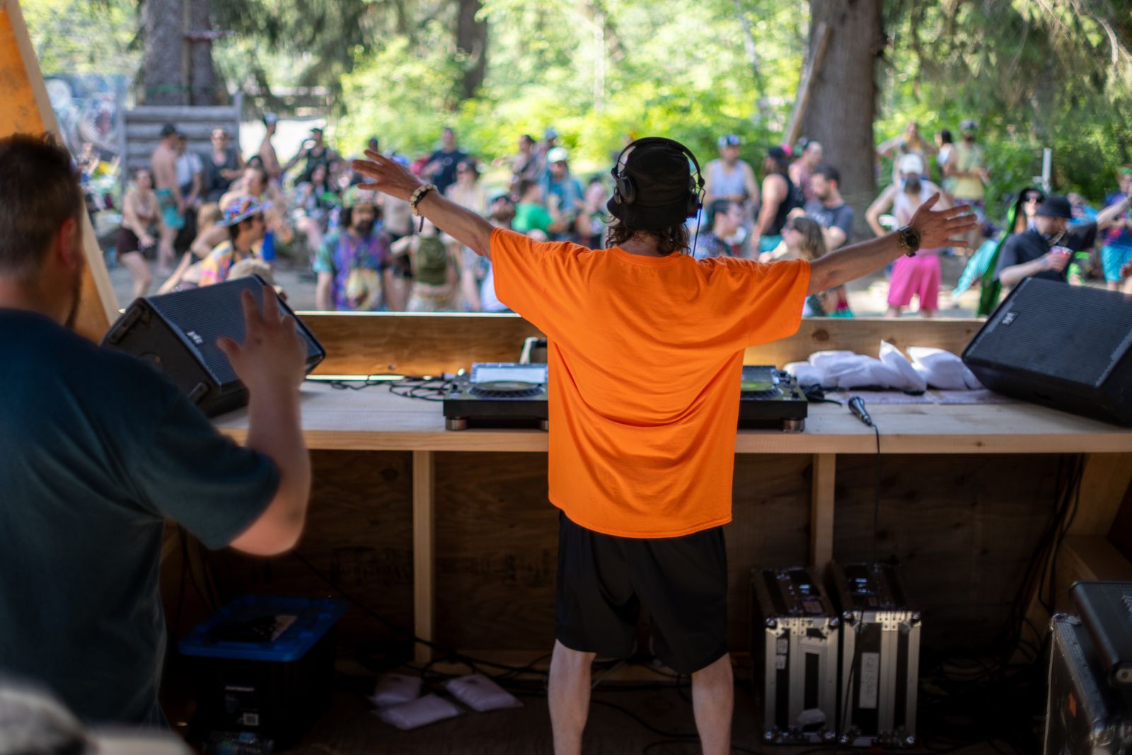 DJ in orange shirt raises arms to crowd