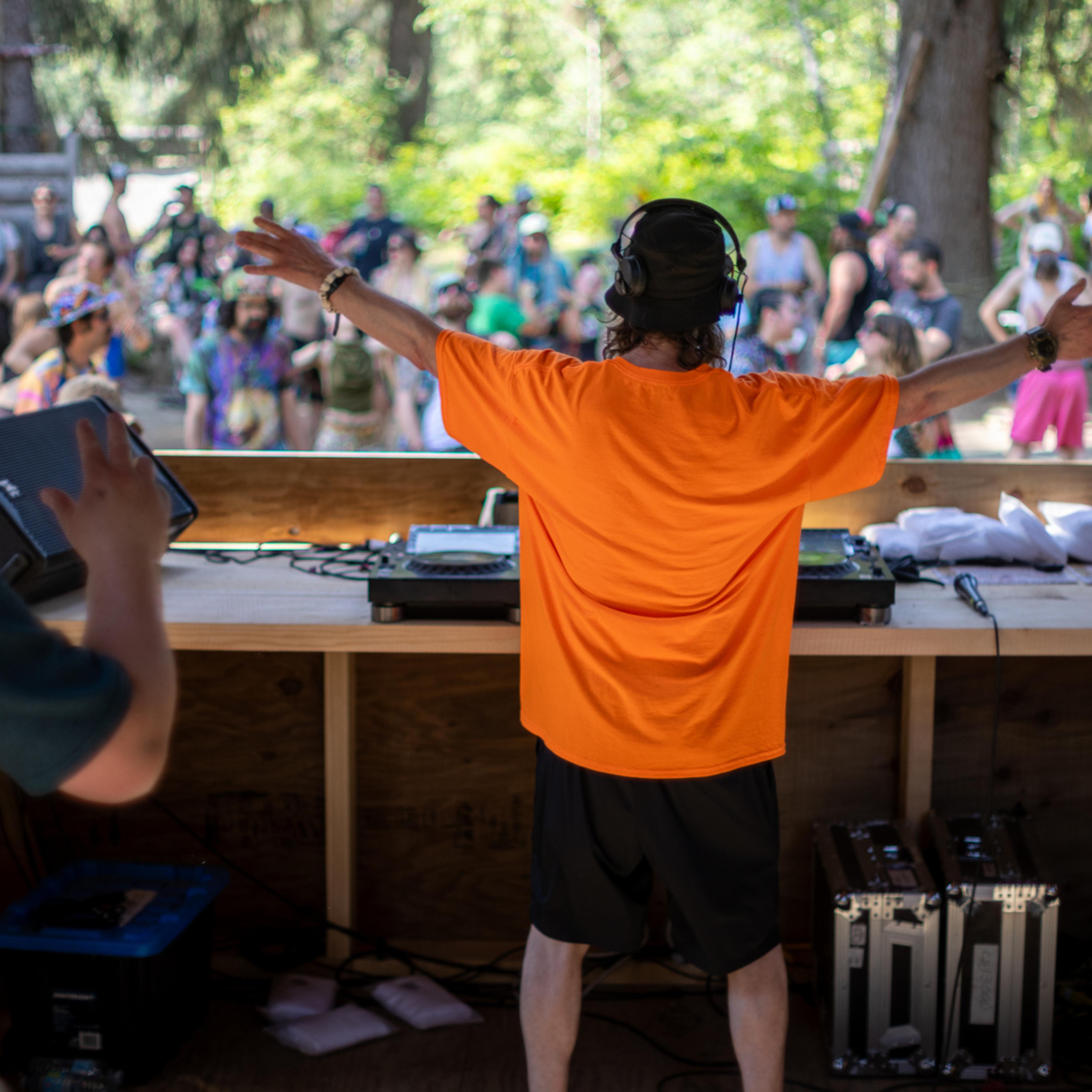 DJ in orange shirt raises arms to crowd