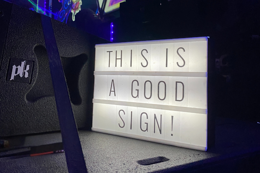 Illuminated light box sign reading 'This Is A Good Sign!' near festival stage at Valhallafest