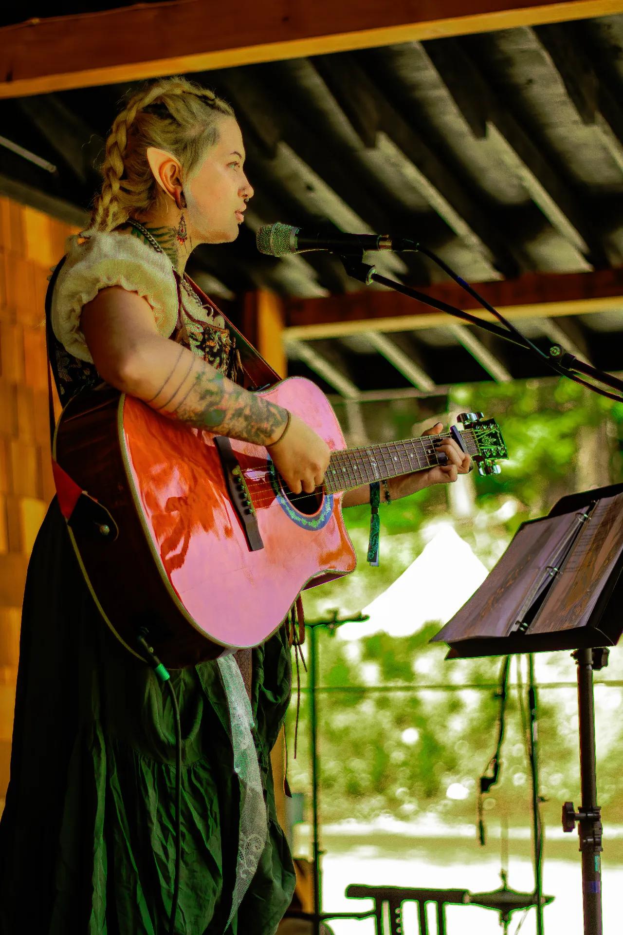 Singer with braided hair performing acoustic set at AgeHa stage.