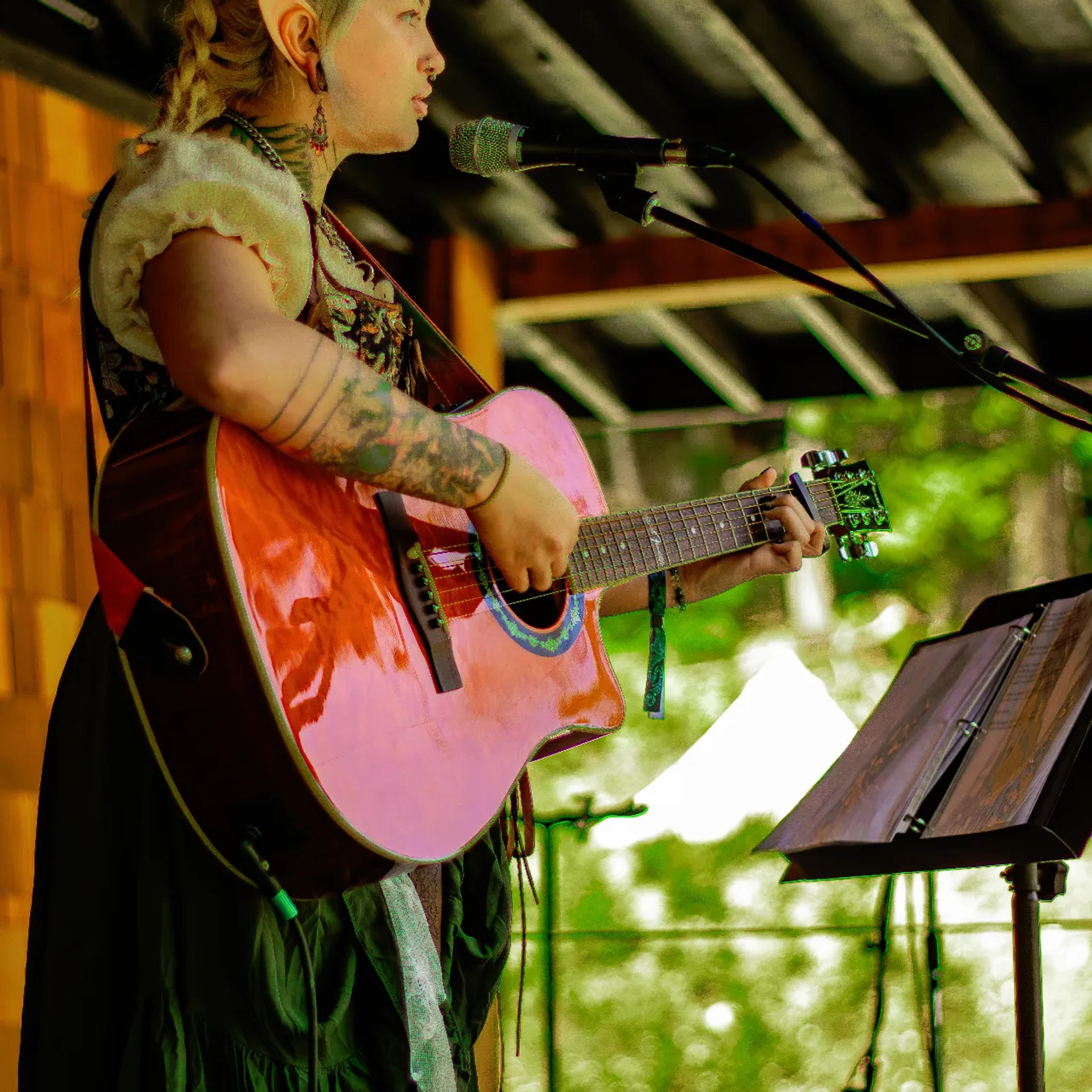 Singer with braided hair performing acoustic set at AgeHa stage.