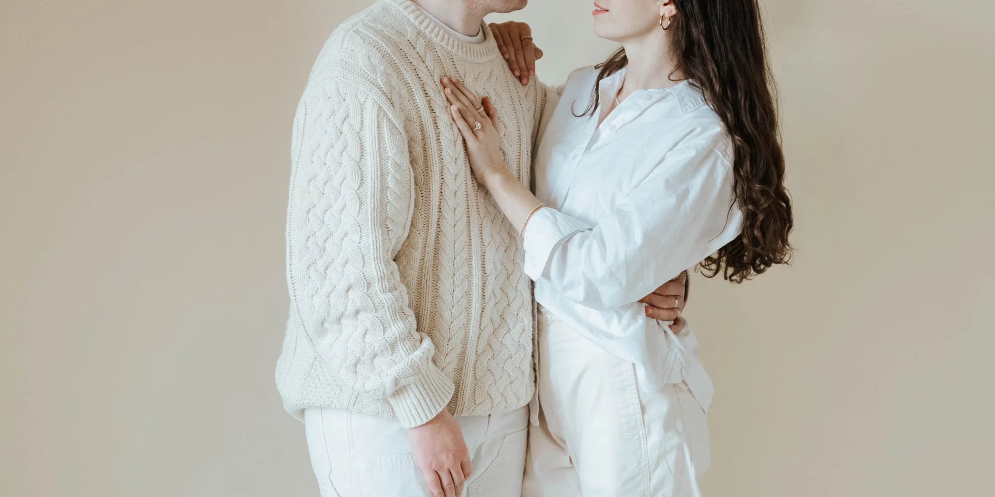 a man and a woman are facing each other. The woman's hand is on the man's chest. Their faces are not visible. The woman's hand has a diamond ring on it.