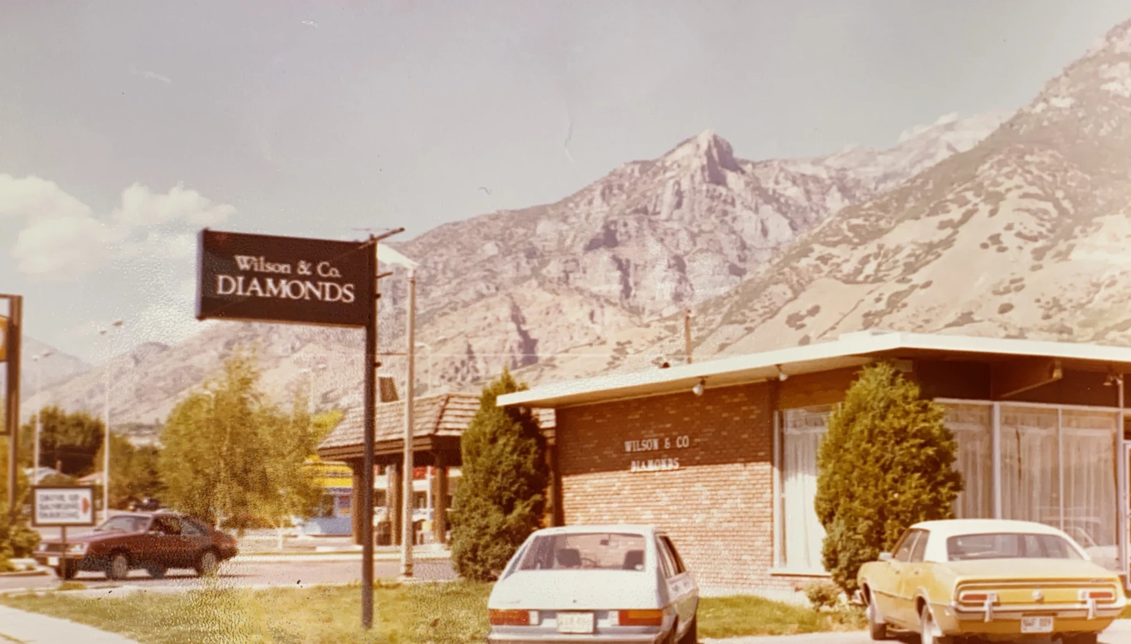 A photo of the first Wilson Diamonds retail location in the 1970s, a small building with a sign that reads 'Wilson Diamonds'. Behind the store are beautiful mountains.