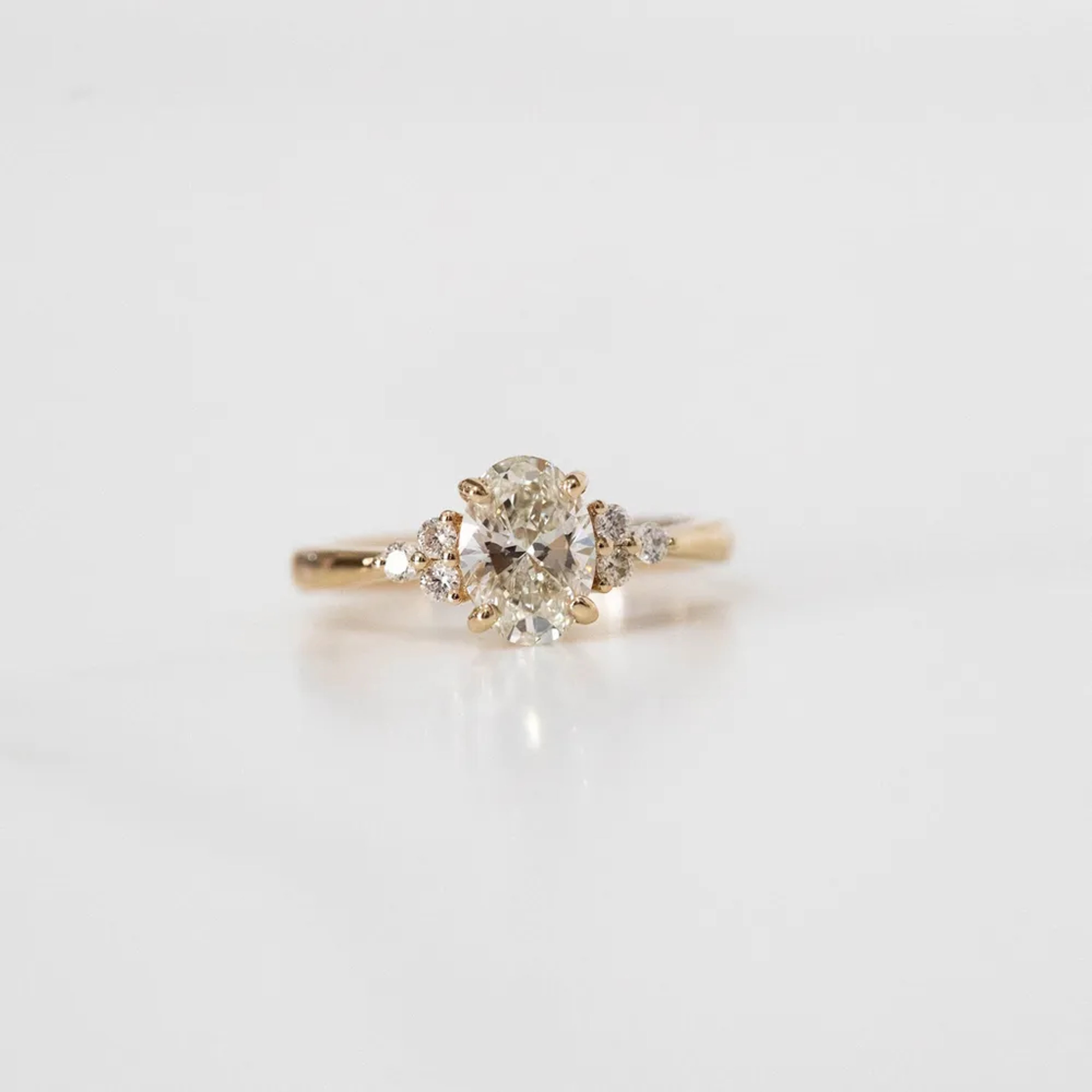 a close-up of a yellow gold, oval-cut diamond ring with a halo of smaller diamonds, against a plain white background