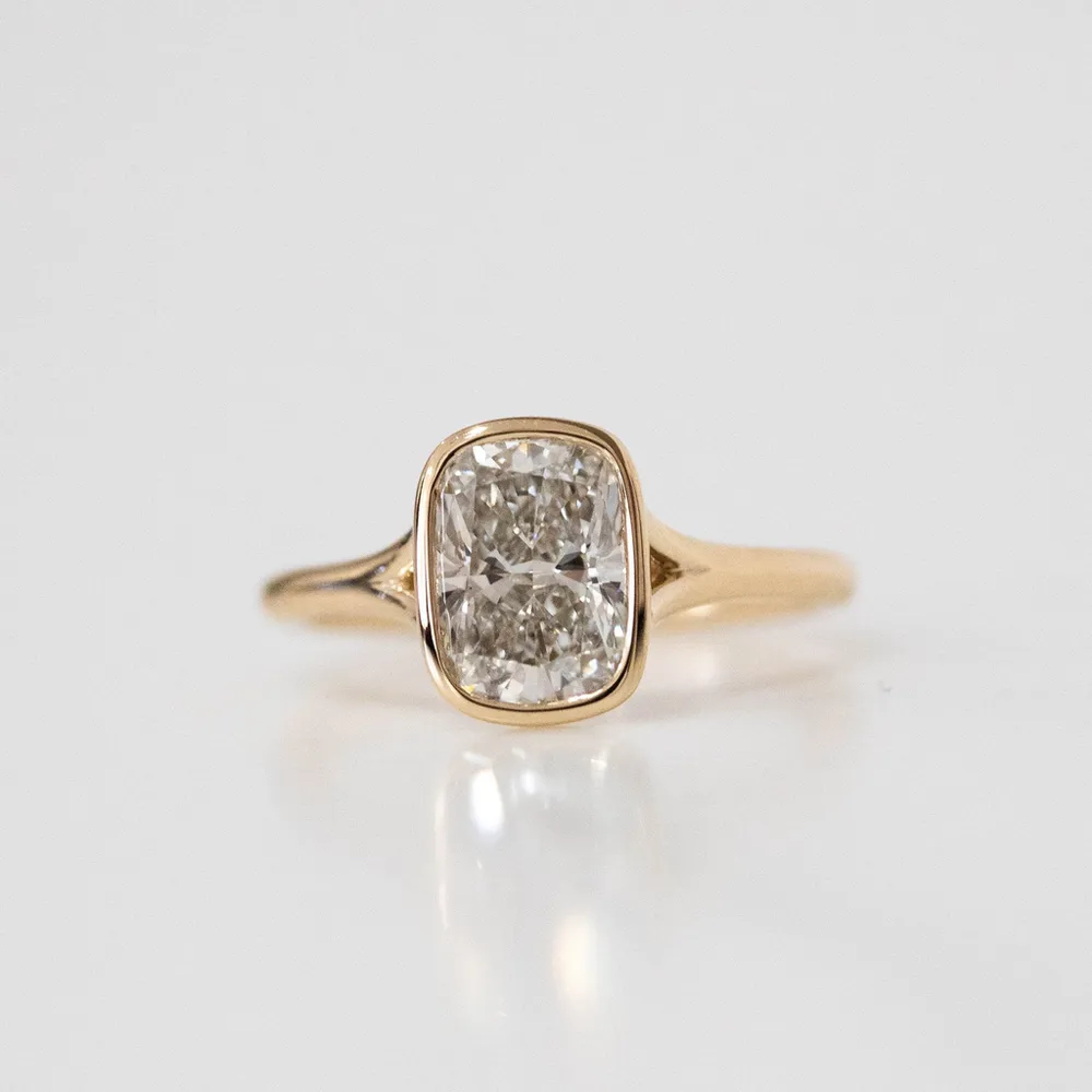 a close-up of a yellow gold, oval-cut diamond ring set into a bezel against a plain white background
