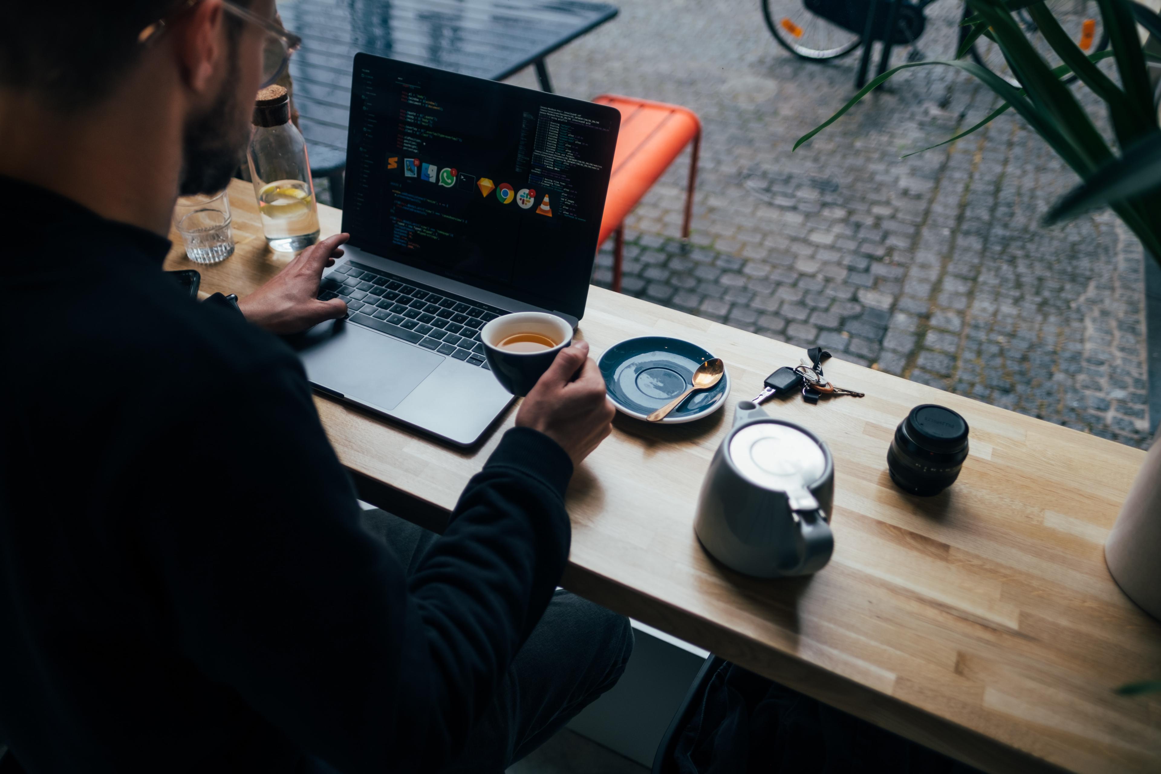 A man multitasking on his laptop while siping a drink. 