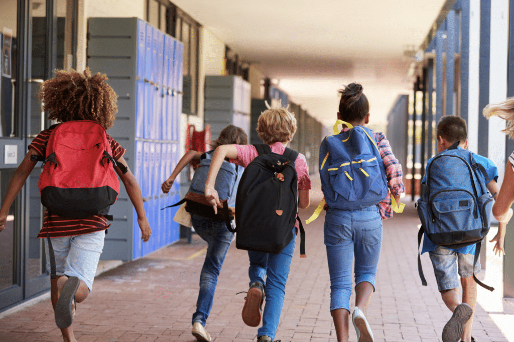 a group of children with backpacks are running down a hallway