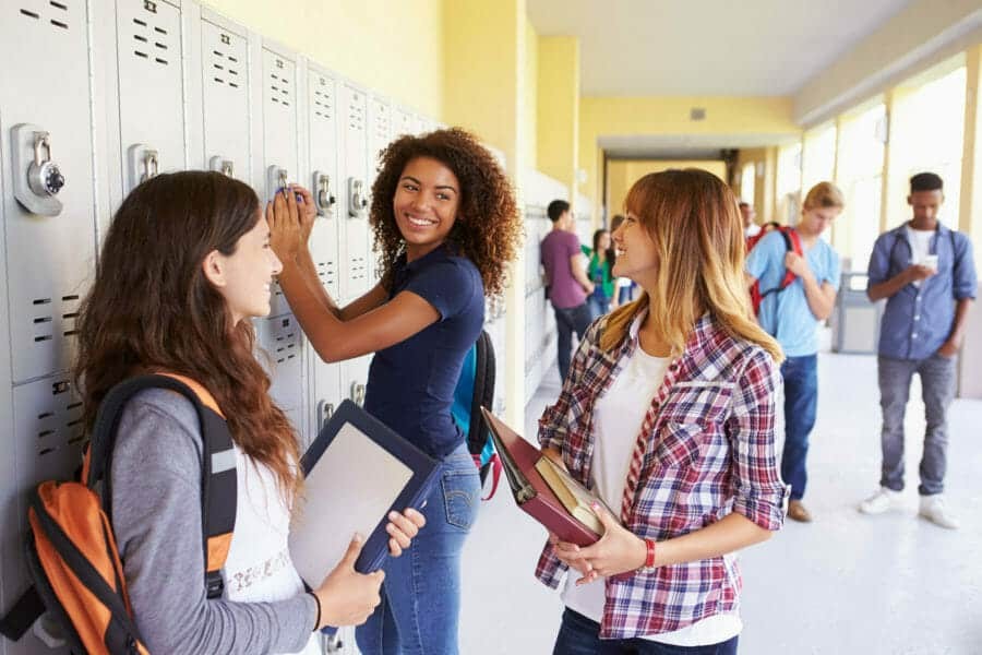 a group of students are standing next to lockers in a hallway .