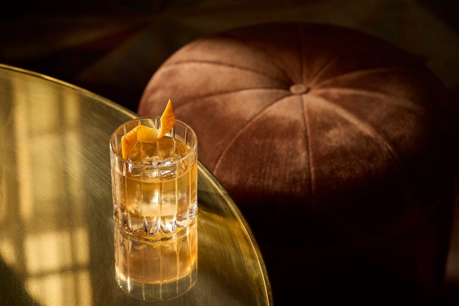 An Old Fashioned cocktail with an orange twist on a brass table at Gaucho