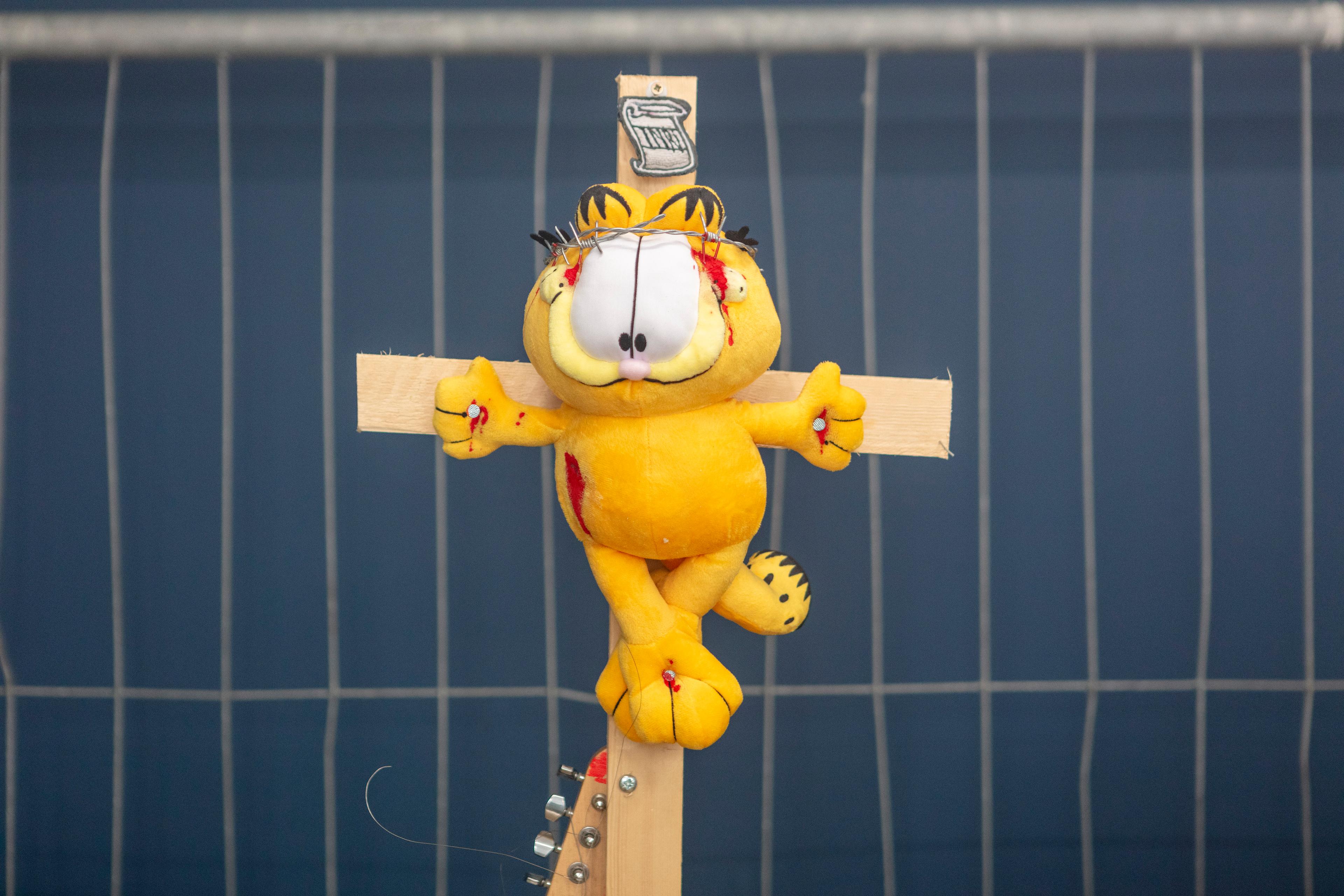 Een Garfield knuffel is gespijkerd op een houten kruis. 