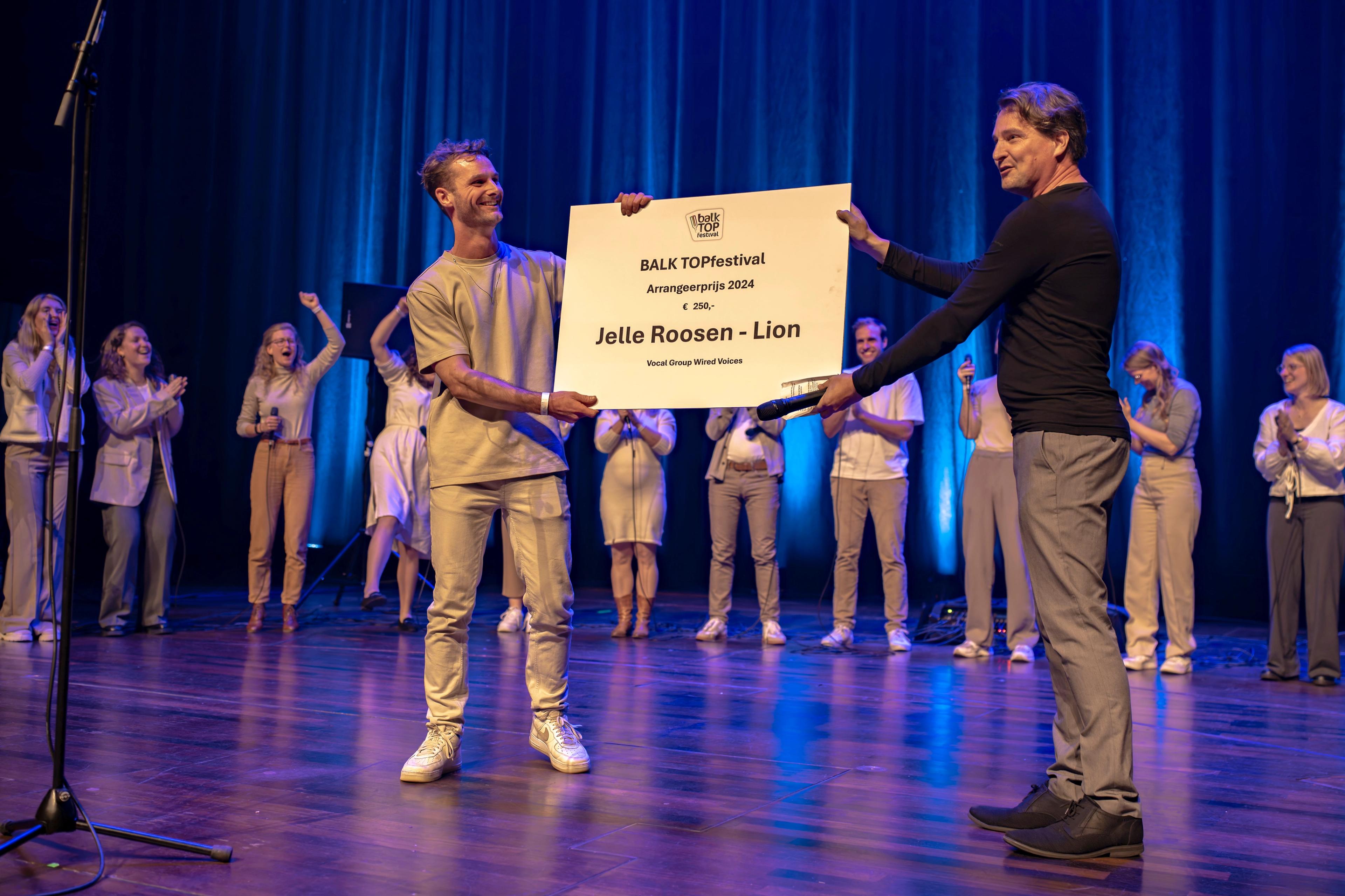Jelle ontvang de Arrangeerprijs en neemt op een podium een grote cheque in ontvangst.