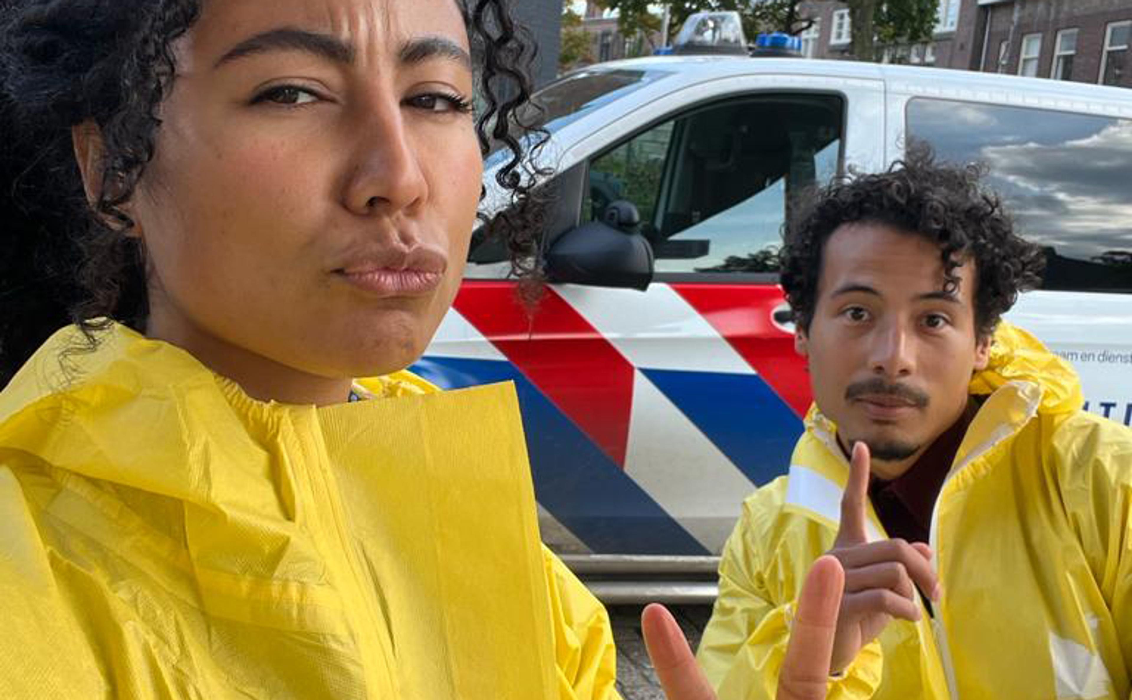 Beelden uit de YouTube serie, de presentatoren staan in gele pakken voor een politiebusje.