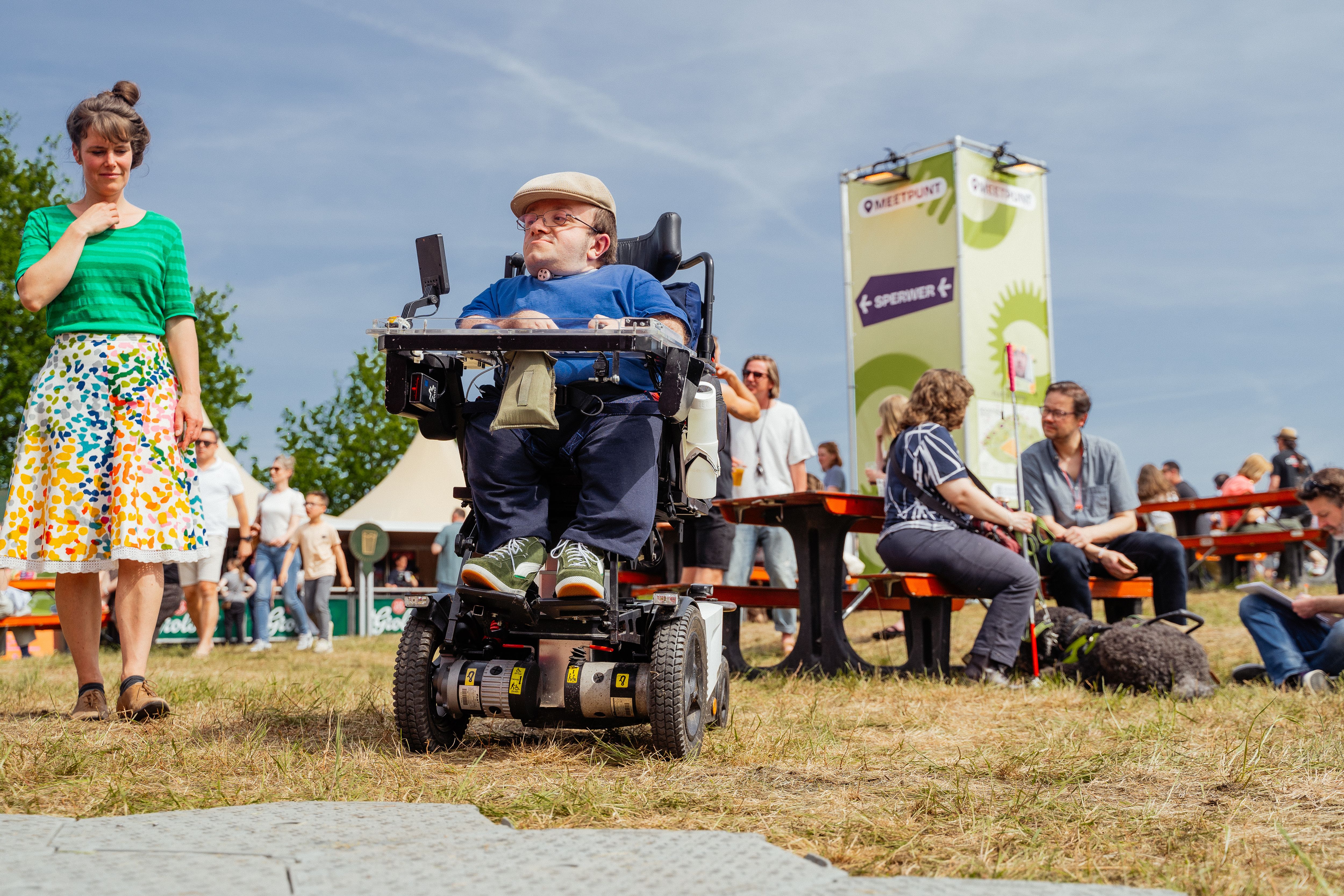 Foto van een festivalbezoeker die in zijn rolstoel het festivalterrein op rijdt.