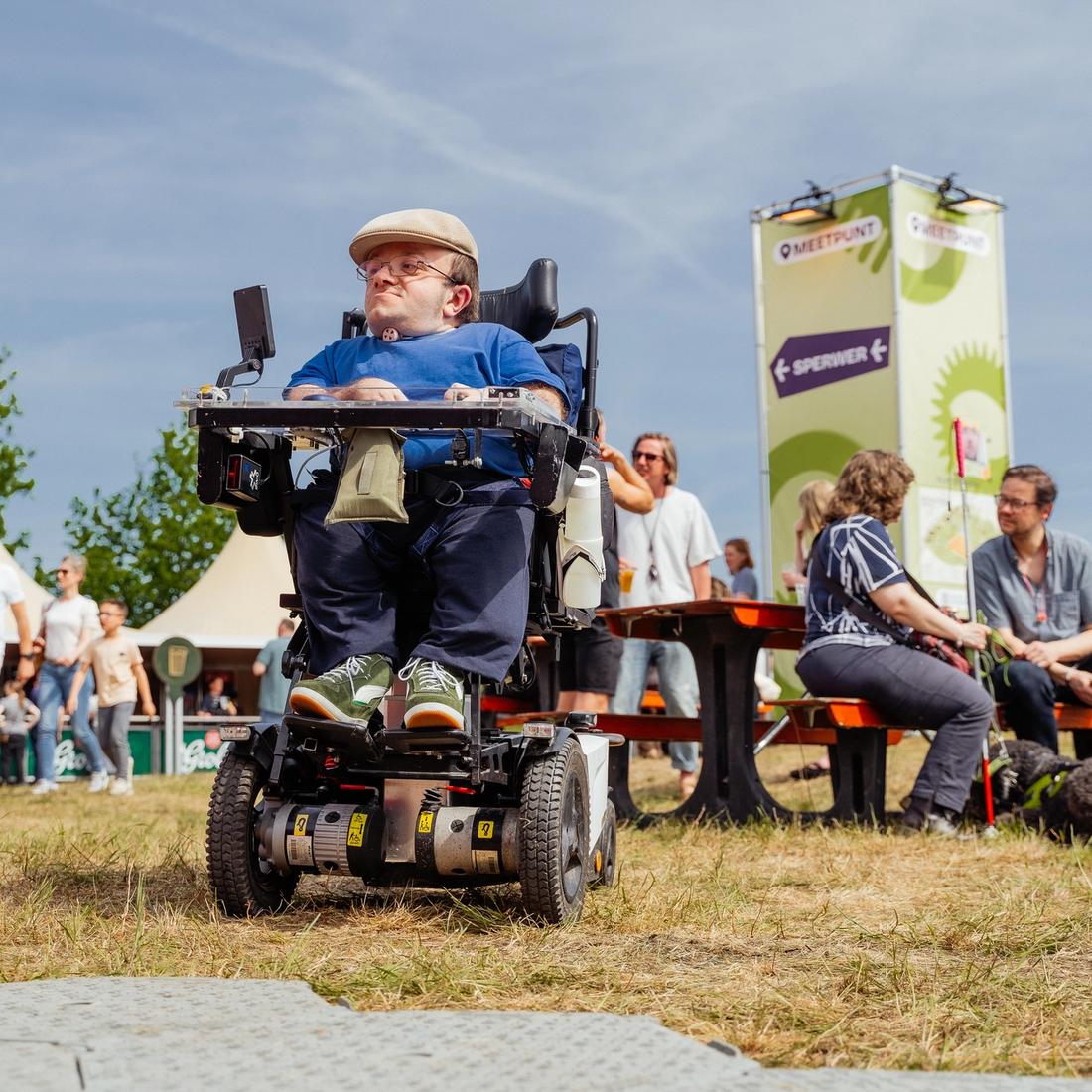 Foto van een festivalbezoeker die in zijn rolstoel het festivalterrein op rijdt.