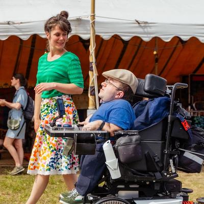 Photo of two people at a festival, one of whom is in a wheelchair