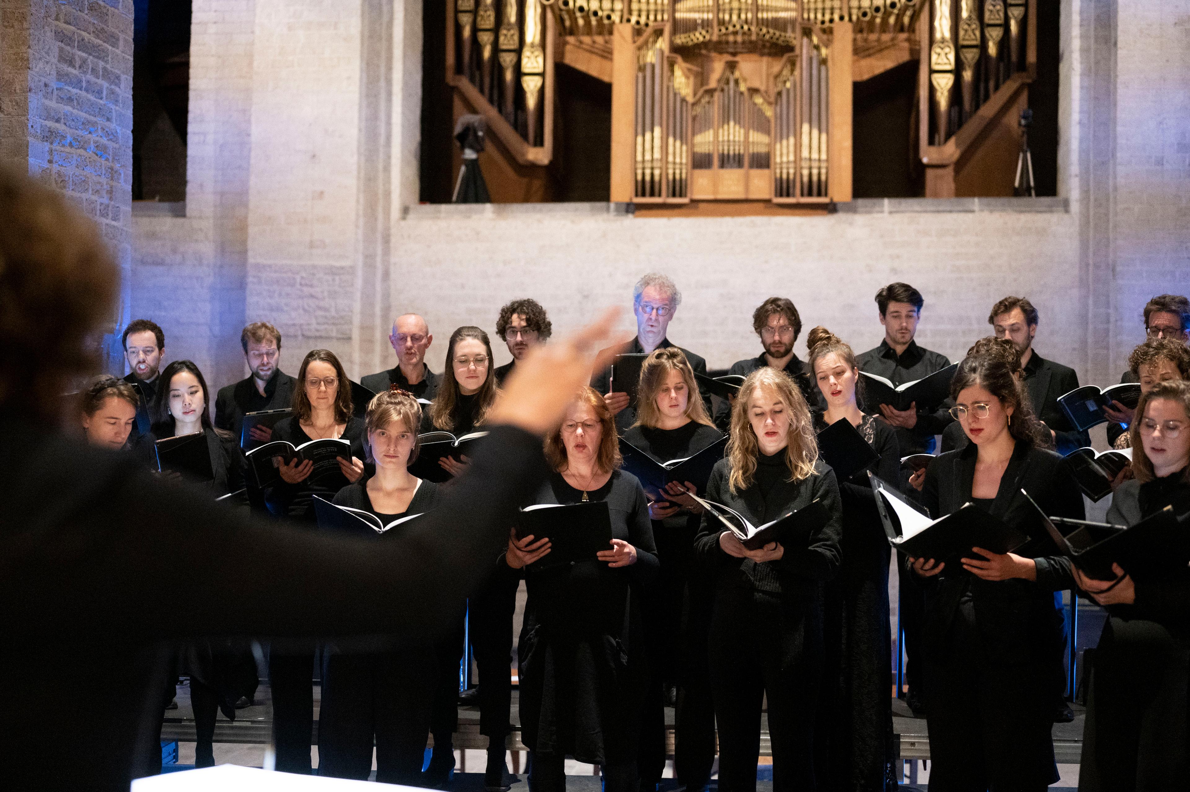 Een foto waarop je de dirigent en het koor bezig ziet.