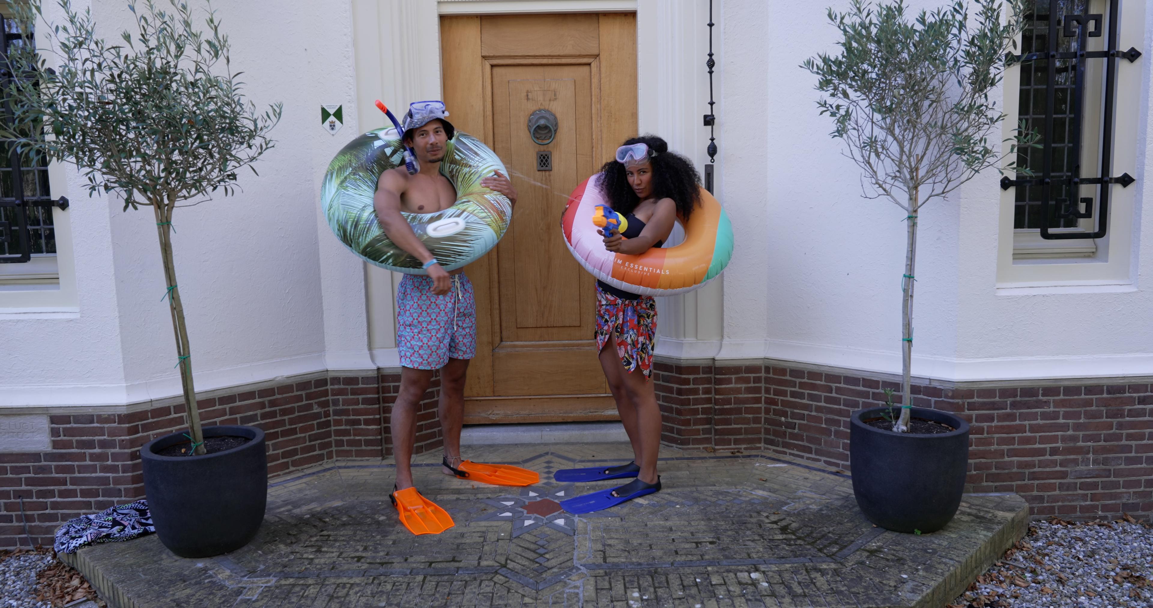 Beelden uit de YouTube serie, de presentatoren staan in zwemkleding met flippers en een zwemband voor een huis.