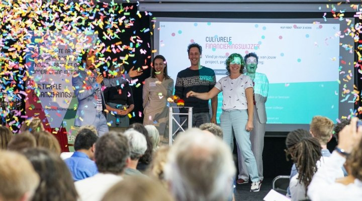 Foto van zes mensen om een rode knop, met confetti in de lucht