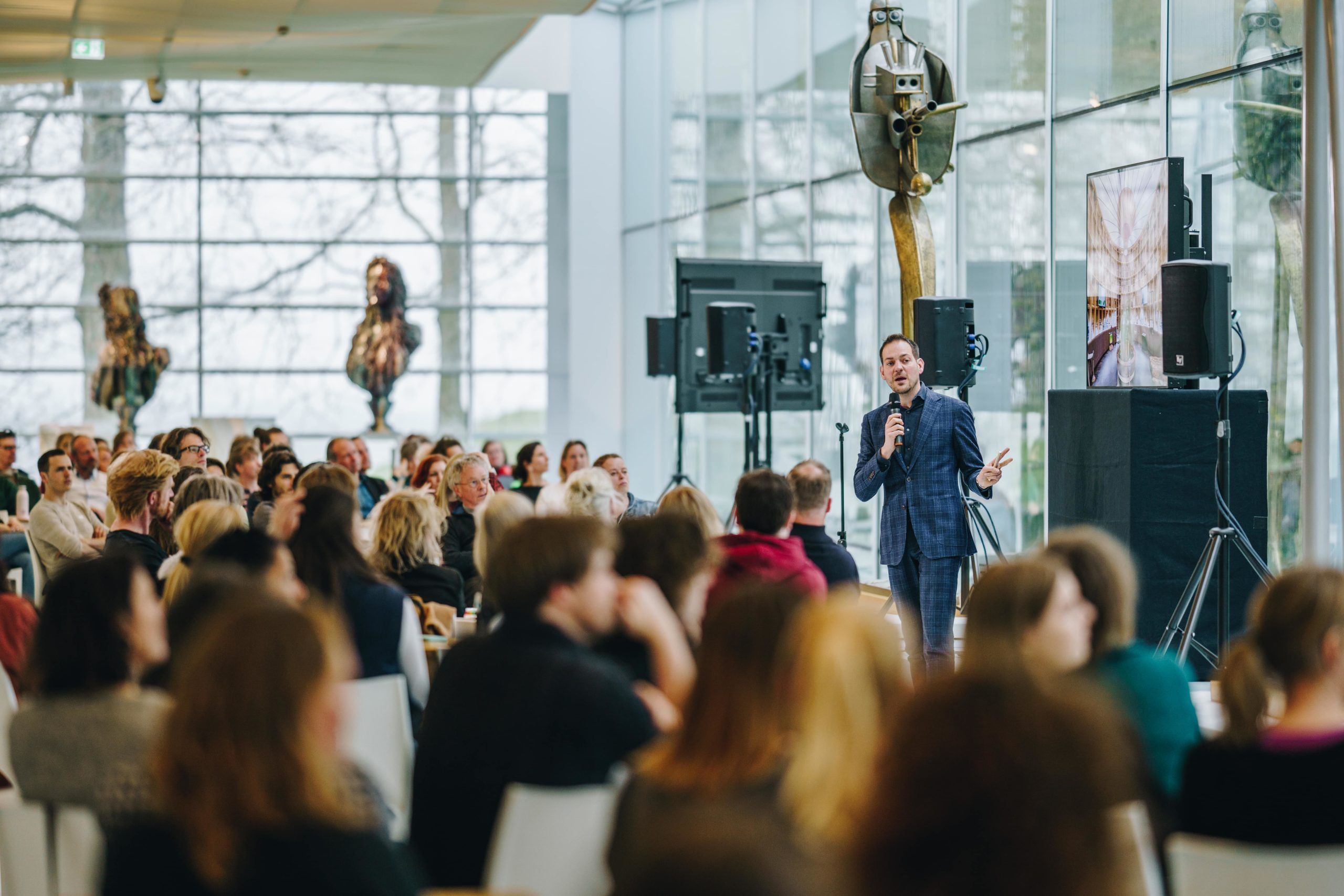 Foto van Lucas de Man, sprekend op een podium voor een zal vol mensen