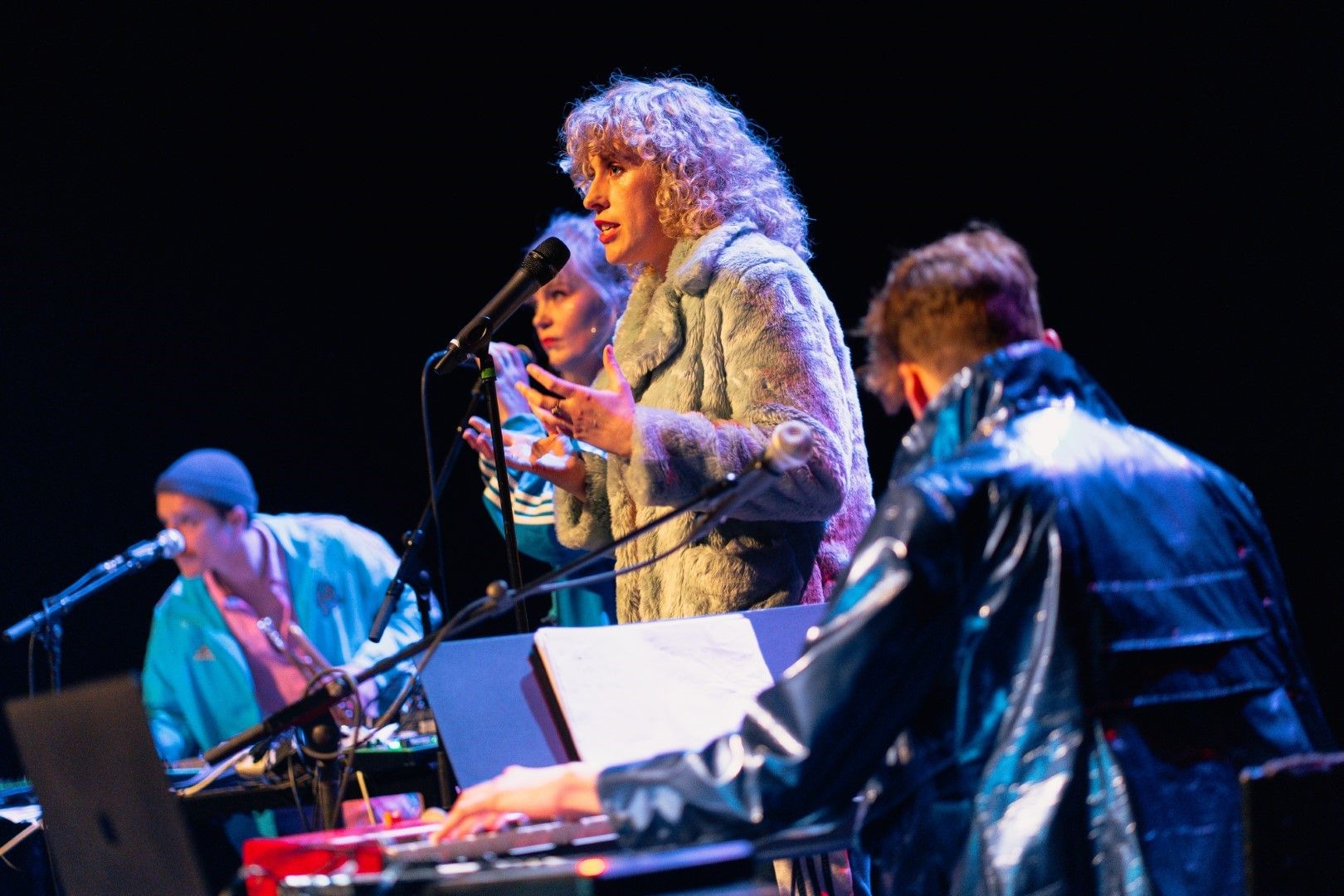 Vrouw staat bij microfoon op een podium met muzikanten om haar heen.