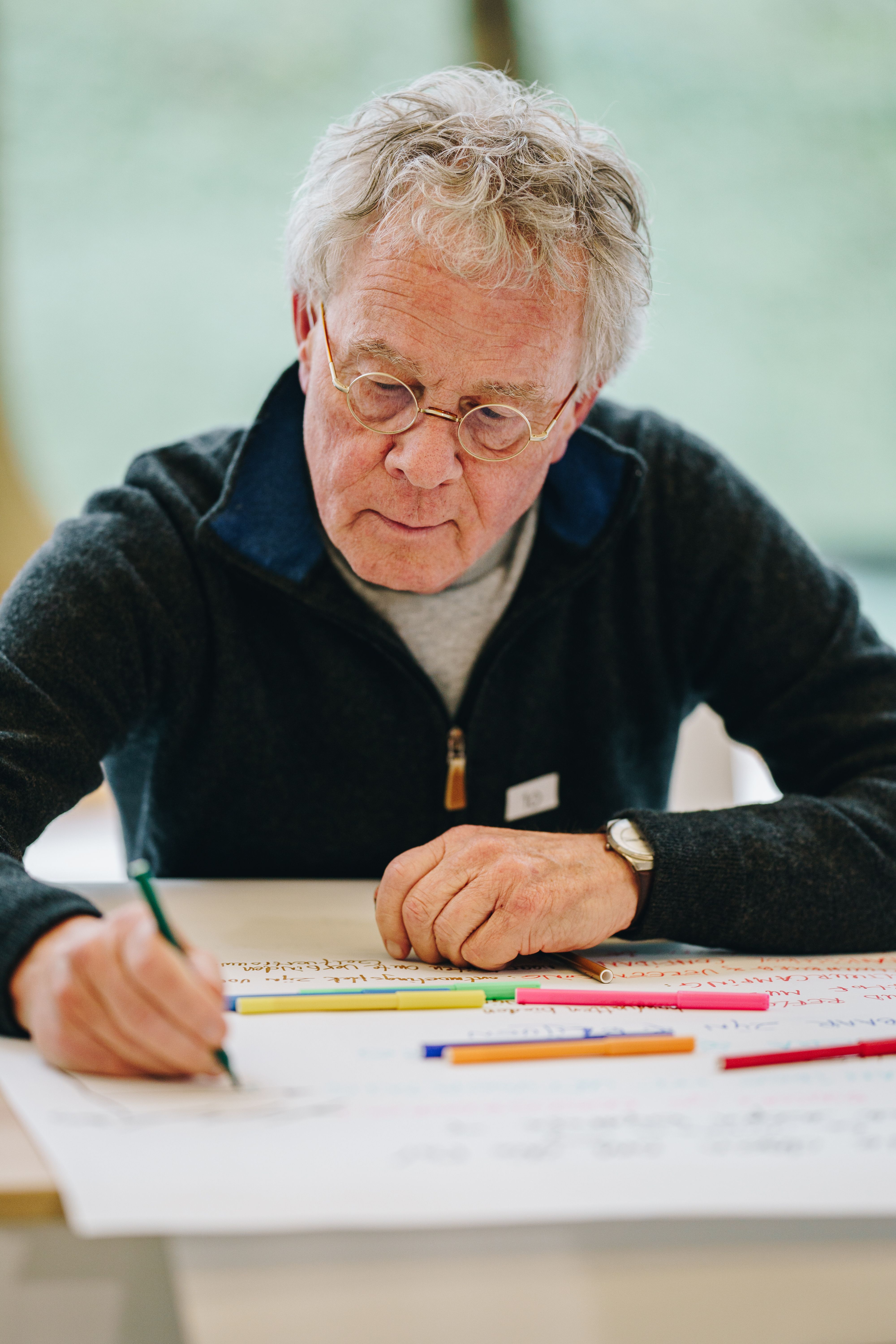 Oudere man met bril die een plan maakt op een groot vel papier met verschillende kleuren stift.